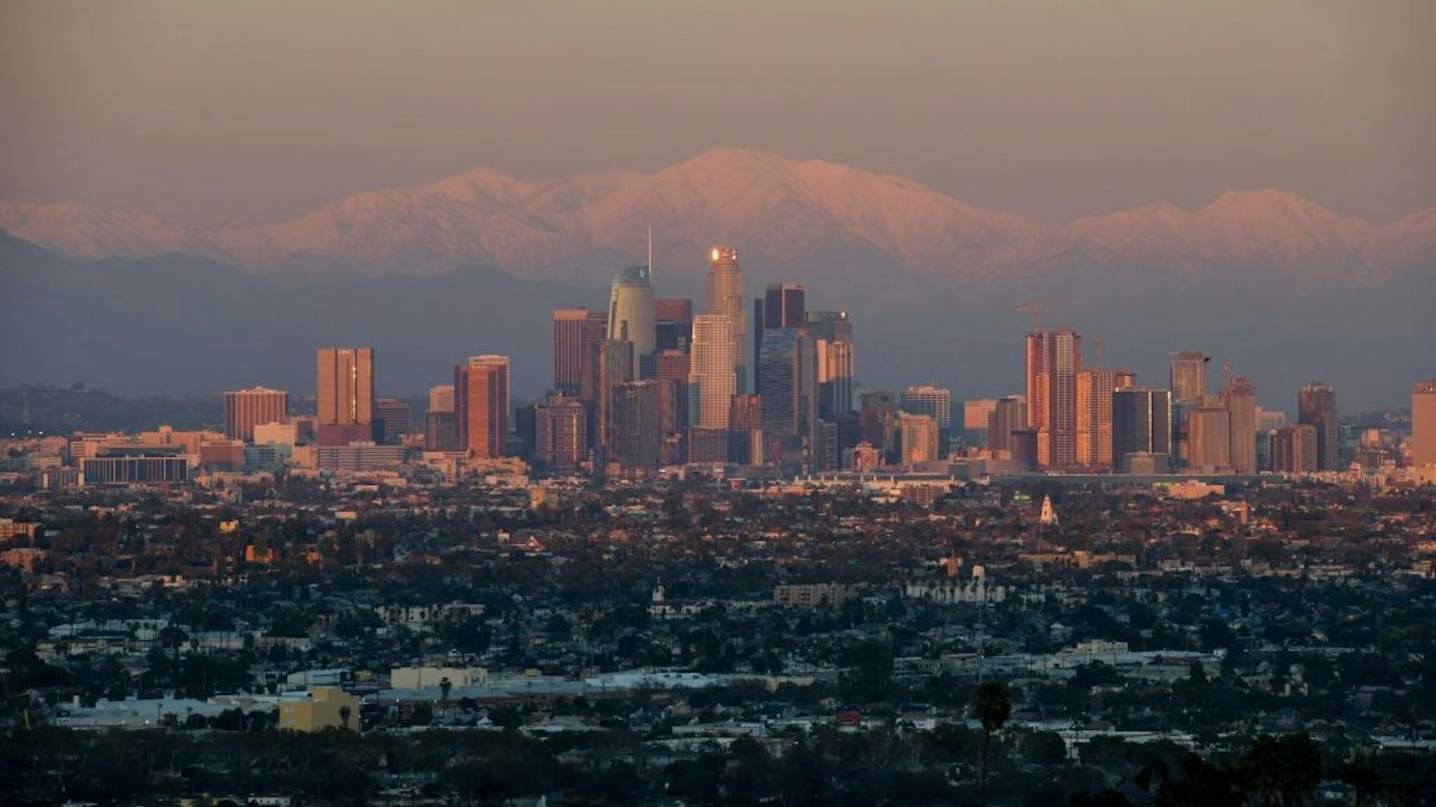 This photo shows a view of the downtown Los Angeles skyline with the snow-covered San Gabriel Mountains in the background as the sun sets on February 7, 2019.