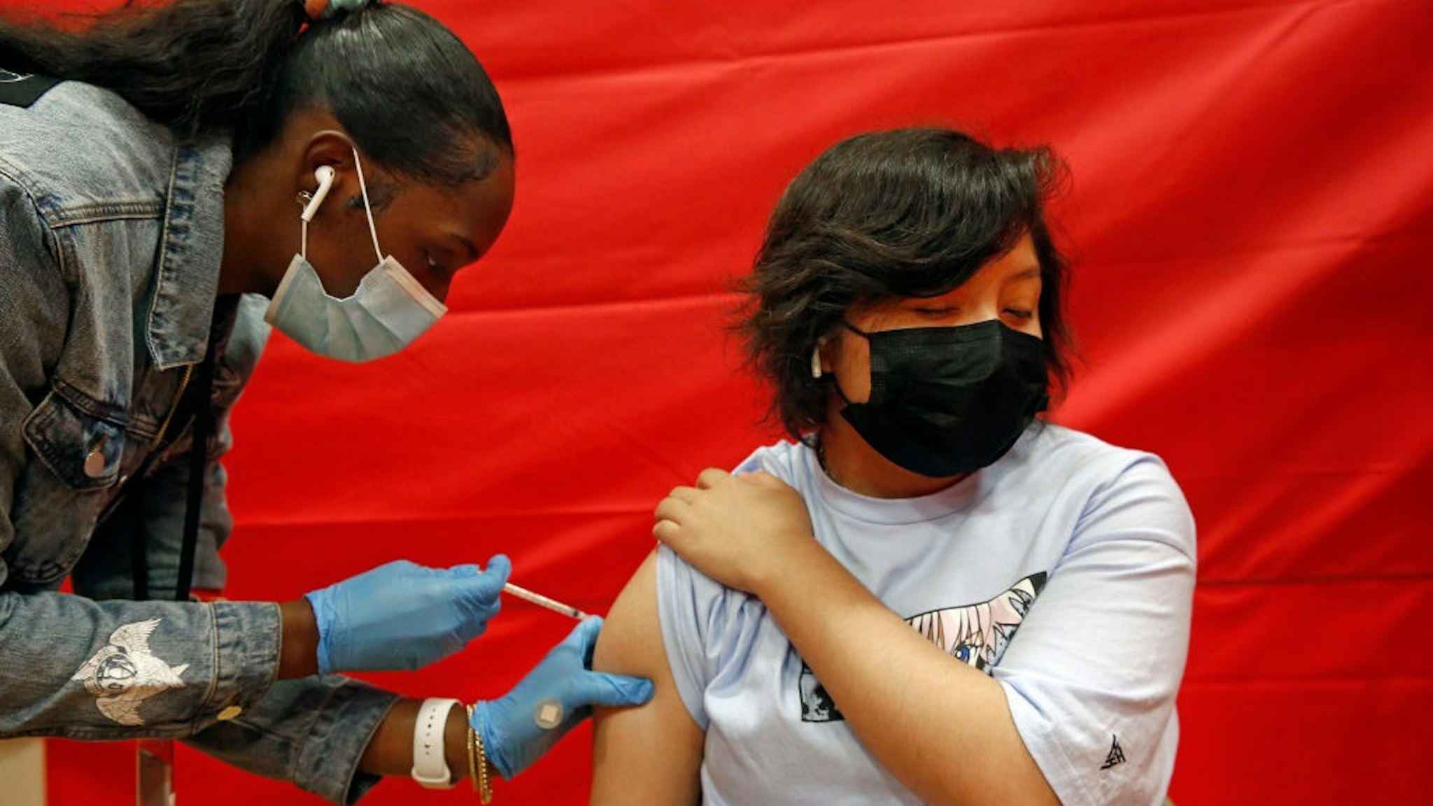 LOS ANGELES, CA - MAY 17: Alex Olvera, 15, is vaccinated with Pfizer by Rickeyva Foster, left, at the Manual Arts High School basketball and gym building in downtown on Monday, May 17, 2021 in Los Angeles, CA. The school is one of 200 sites that the Los Angeles Unified School District has deployed mobile vaccination teams to get as many shots into students arms as possible.