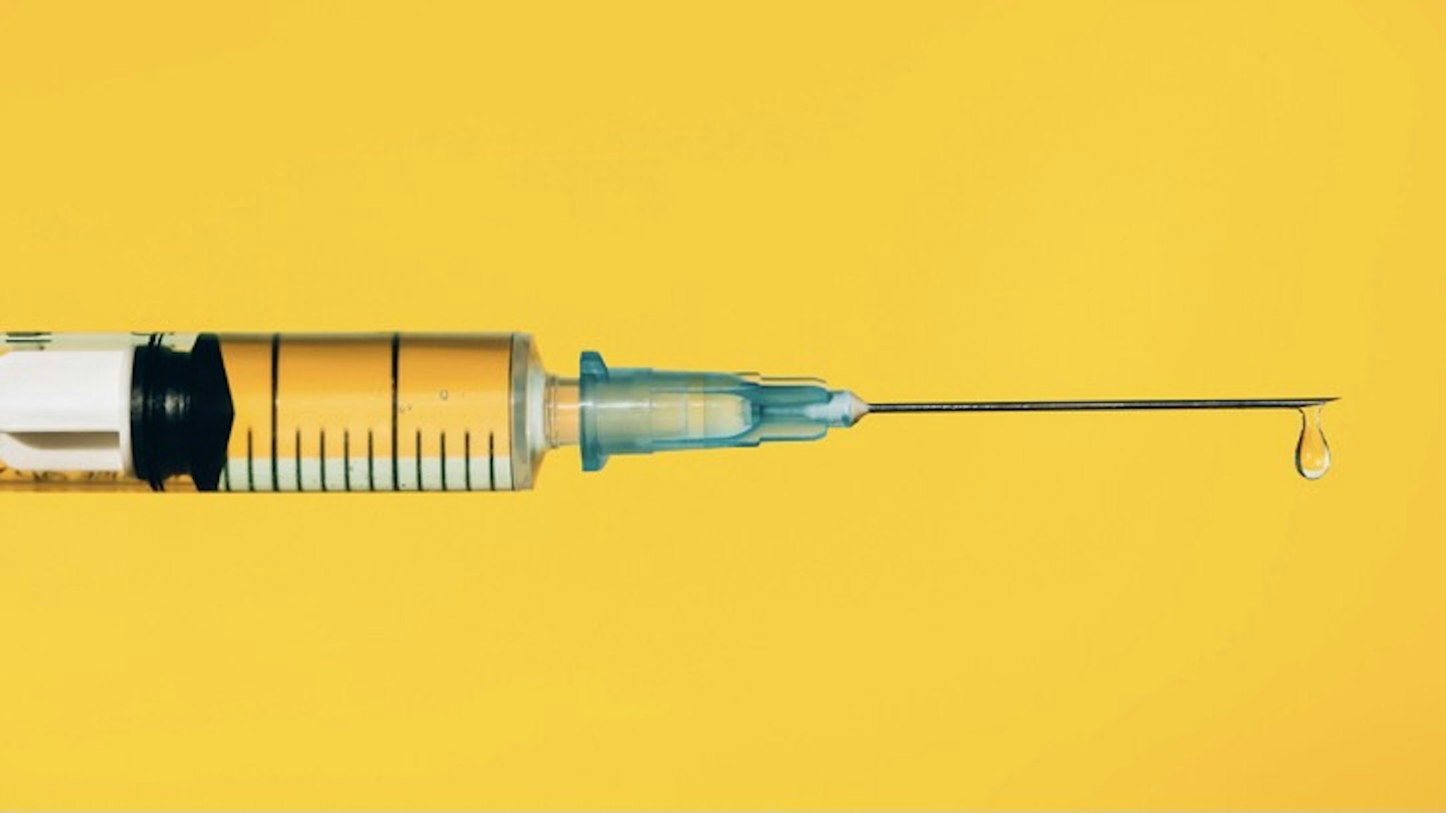 Modern syringe with liquid drug. The most anticipated procedure of the year - stock photo Closeup contemporary disposable syringe with drop of fluid medication on needle placed against vivid yellow background. Vaccination is the most anticipated procedure of the year. Research of coronavirus disease protection concept. Covid-19 vaccine studies. Anna Efetova via Getty Images