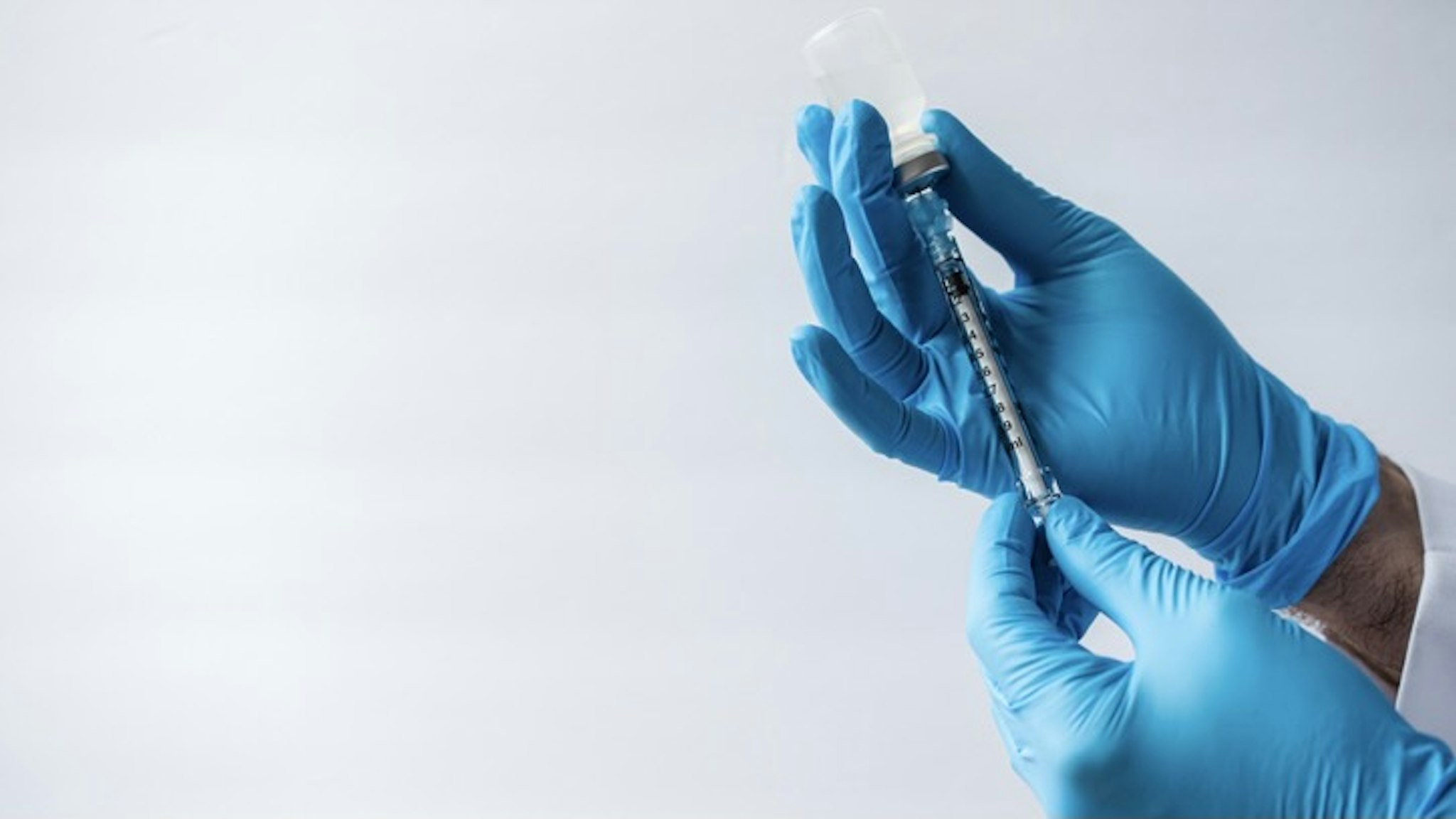 Hands in gloves drawing vaccine into syringe on white background. - stock photo Cavan Images/Getty Images