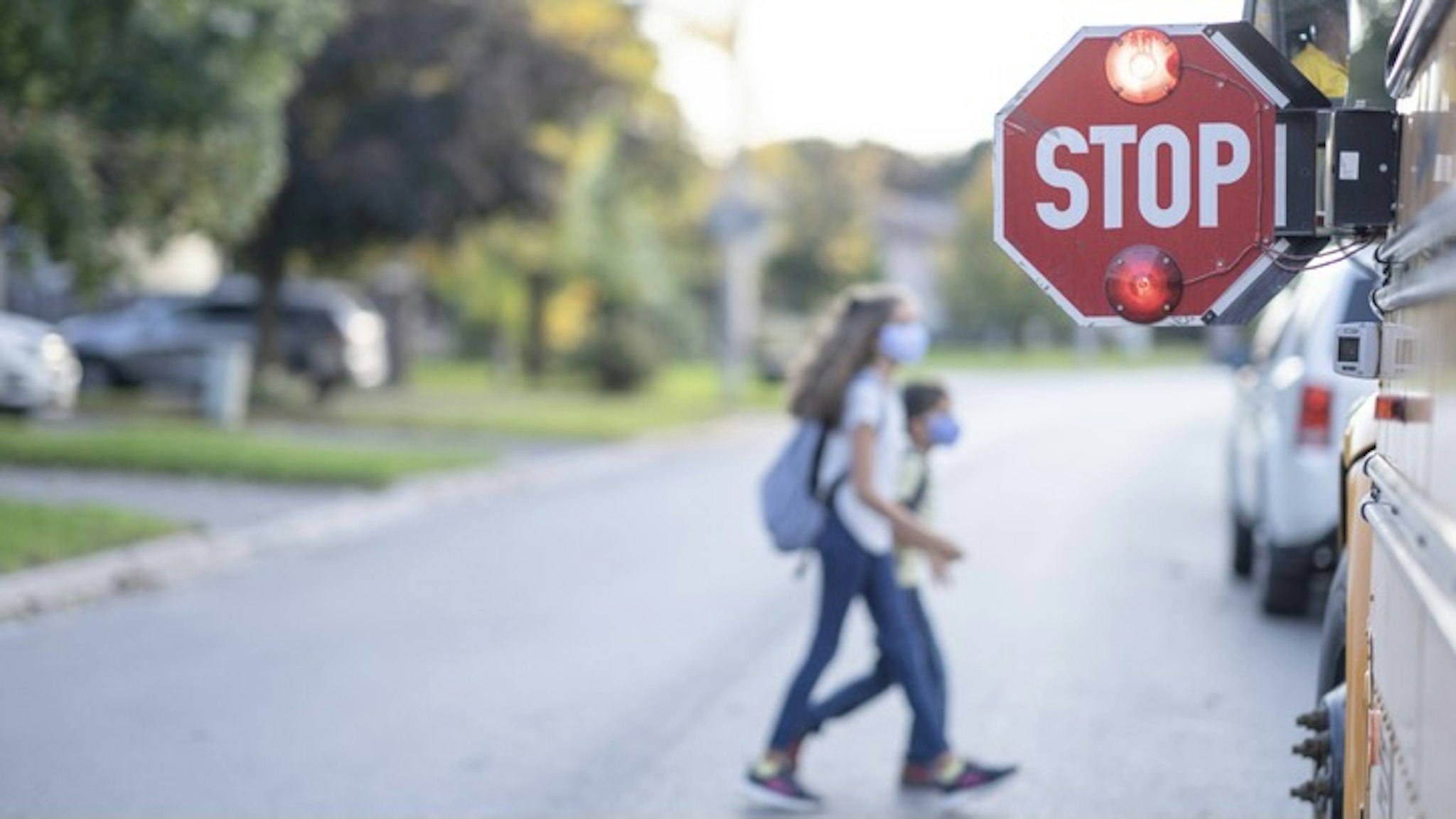 School bus stop sign for children to pass - stock photo A STOP sign is out by the school bus and children can be seeing crossing the road in front of the school bus. FatCamera via Getty Images