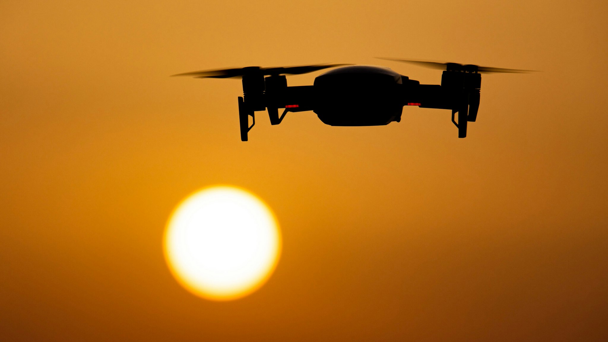 A quadcopter drone hovering during a flight in front of the sun. The flying drone is seen as a dark silhouette against the spectacular colorful sunset sky and the sun while the UAV is able to capture aerial videography and photography via a remote control. The specific drone is a DJI Mavic Air. The Unmanned aerial vehicle is popular for recreational usage by tourists as the technology is accessible to everybody in low cost but also has many professional applications Sani Beach area, Halkidiki, Greece on July 15, 2021