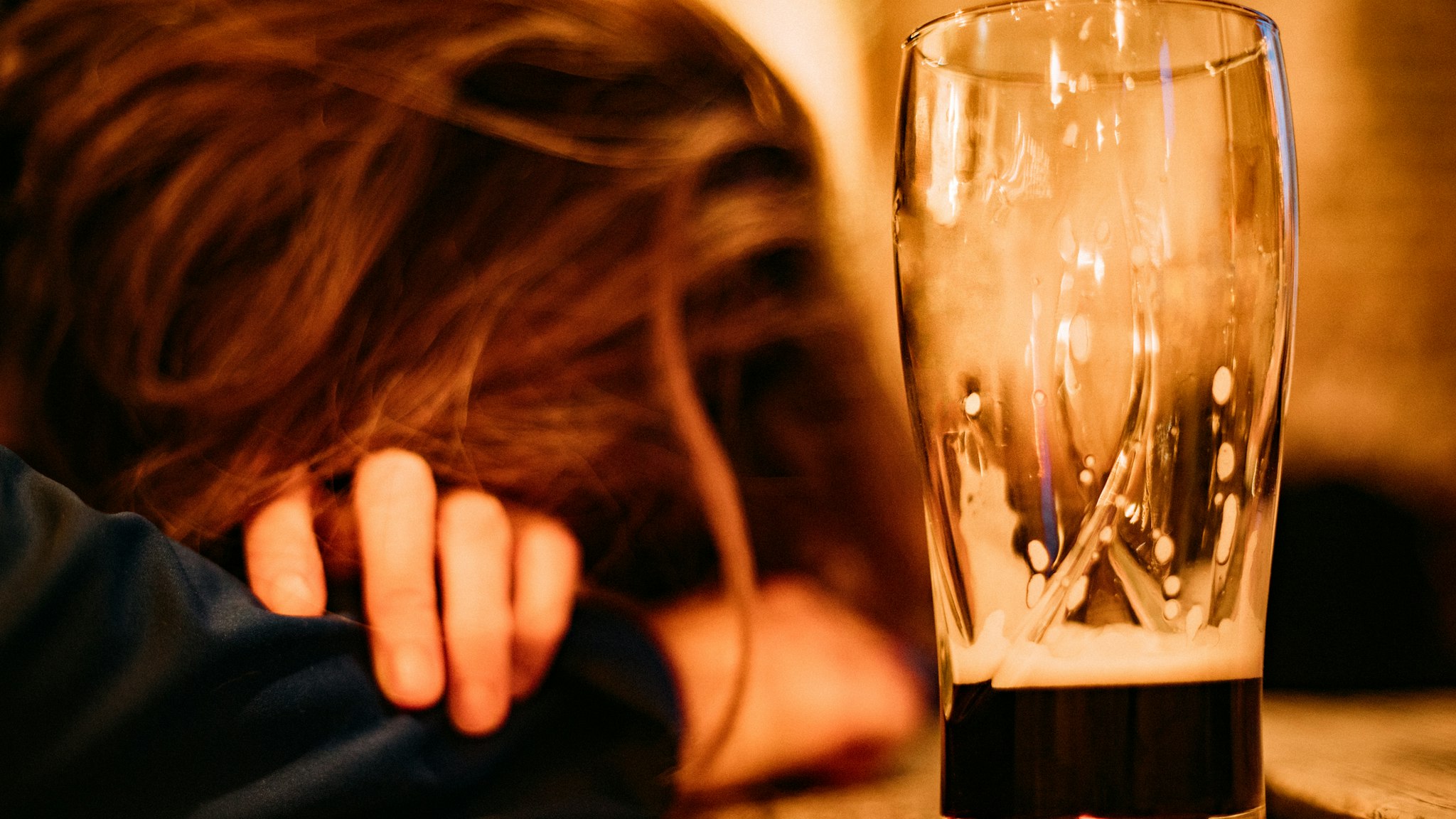 Young drunk woman sleeping on bar counter drinking dark beer - stock photo