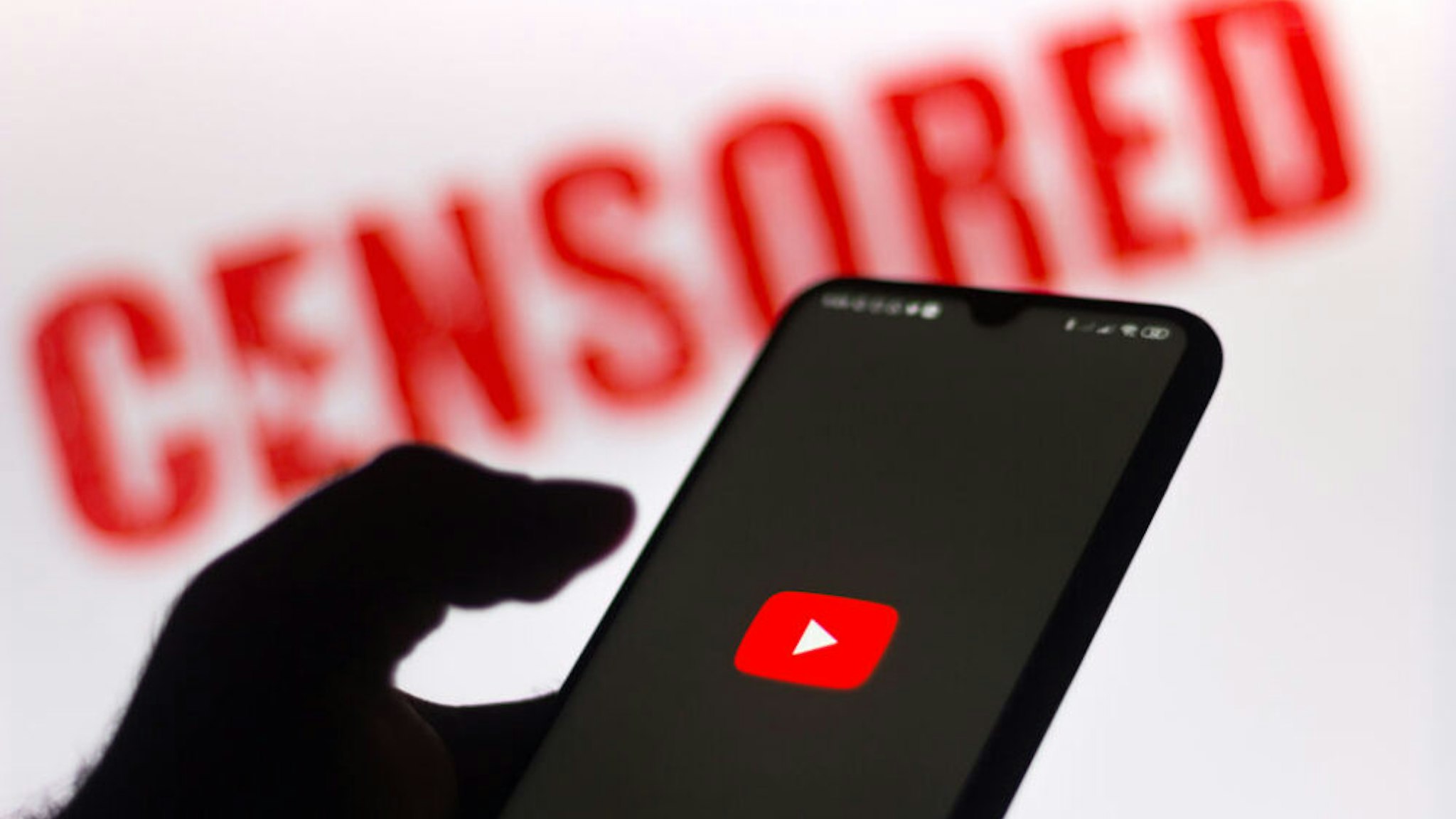 BRAZIL - 2020/06/15: In this photo illustration the YouTube logo is displayed on a smartphone and a red alerting word "CENSORED" on the blurred background.