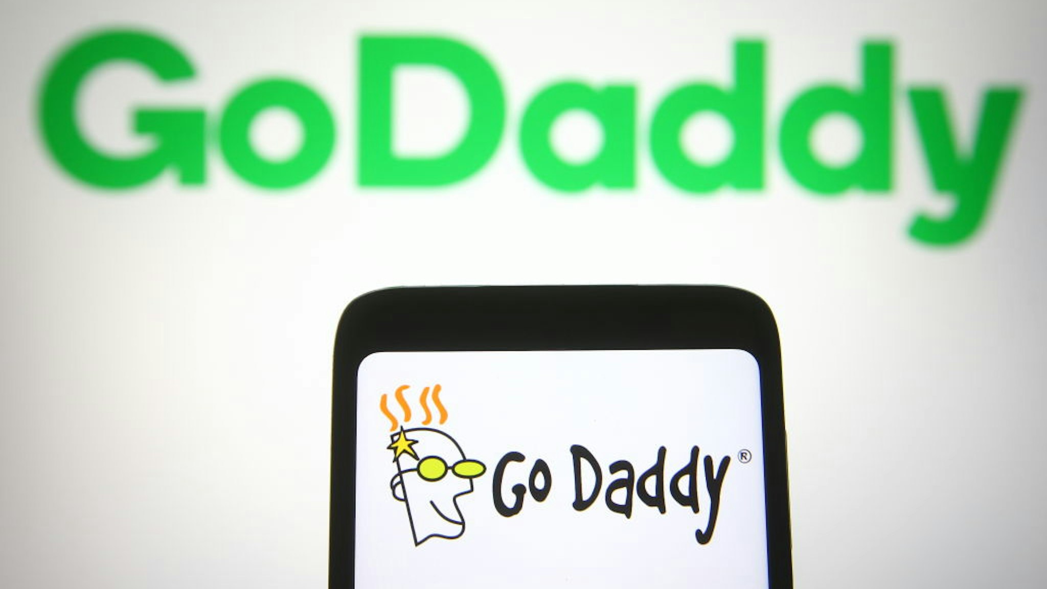 In this photo illustration the GoDaddy logo is seen on a smartphone and a pc screen.