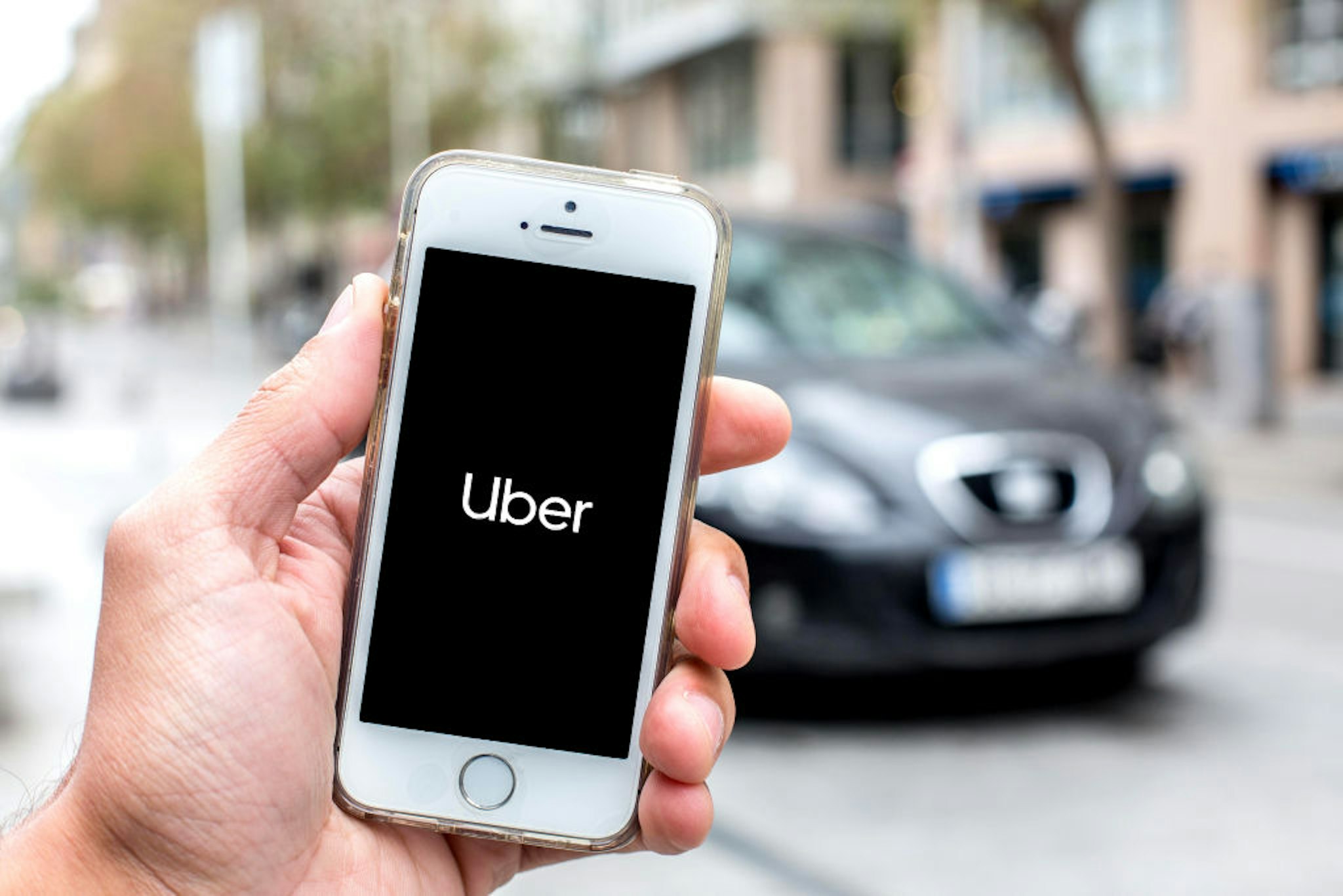 In this photo illustration a Uber logo seen displayed on a smartphone screen with a car in the background.