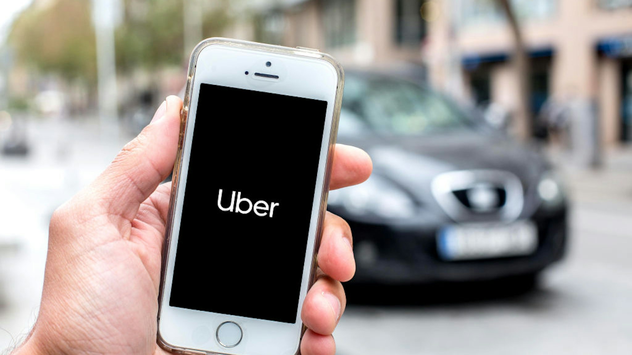 In this photo illustration a Uber logo seen displayed on a smartphone screen with a car in the background.