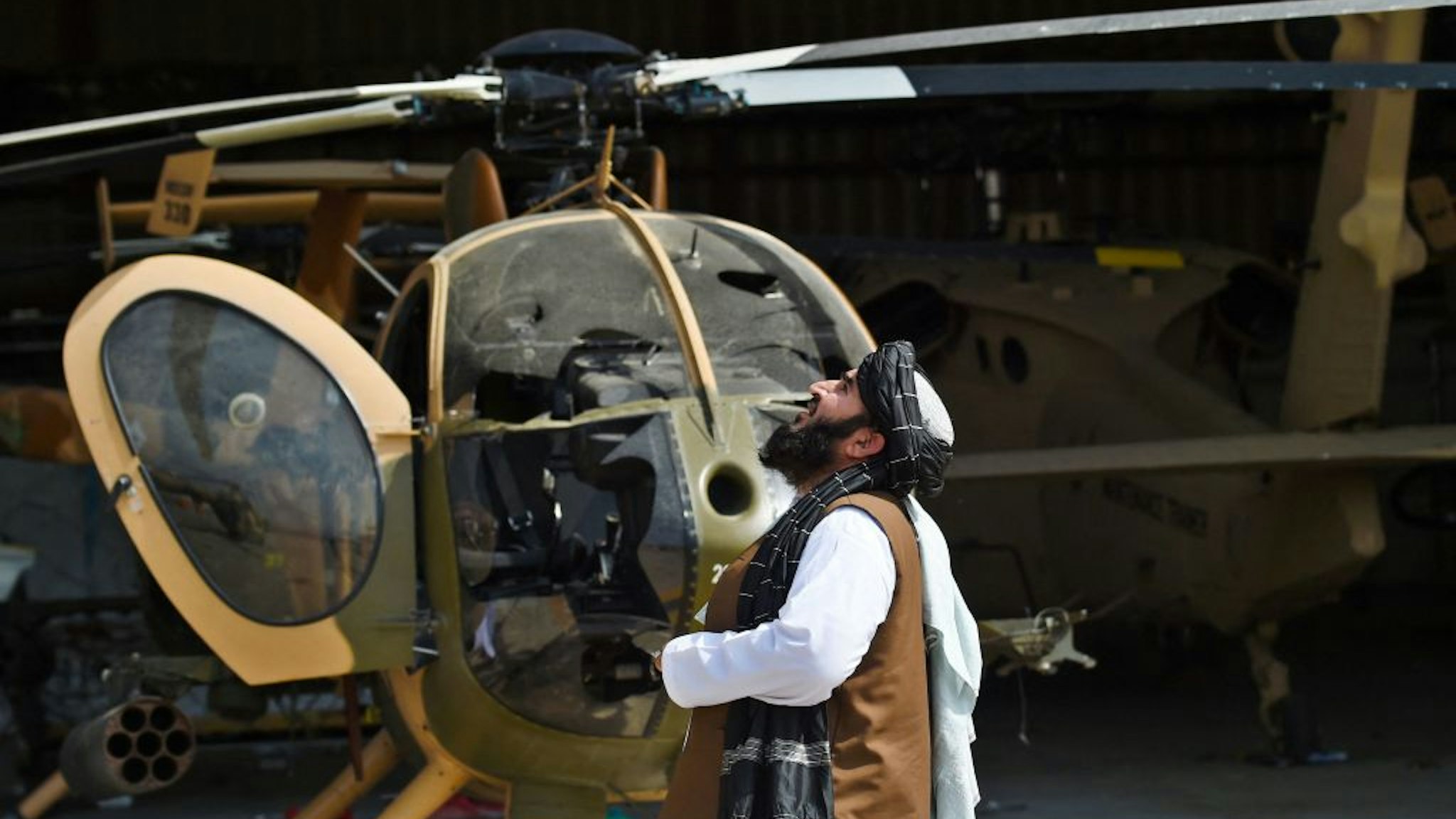 Taliban member looks up standing next to a damaged helicopter at the airport in Kabul on August 31, 2021, after the US has pulled all its troops out of the country to end a brutal 20-year war -- one that started and ended with the hardline Islamist in power. (Photo by Wakil KOHSAR / AFP) (Photo by WAKIL KOHSAR/AFP via Getty Images)