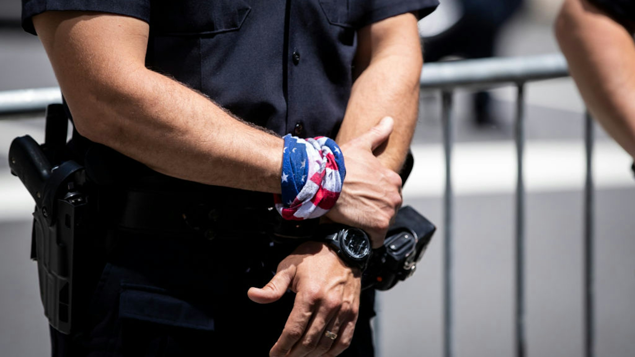 MANHATTAN, NY - JUNE 12: A NYPD officer wears a bandana around his wrist that is of the American flag with his gun at his side stands at the ready to stop any protesters that try to cross the barricade toward Trump Tower cards parked outside of Trump Tower and police officers sand out front in protection against protesters. This was part of the Black Womxn's Empowerment March that started at Trump Tower and marched to Gracie Mansion. Protesters continue taking to the streets across America and around the world after the killing of George Floyd at the hands of a white police officer Derek Chauvin that was kneeling on his neck during for eight minutes, was caught on video and went viral. During his arrest as Floyd pleaded, "I Can't Breathe". The protest are attempting to give a voice to the need for human rights for African American's and to stop police brutality against people of color. They are also protesting deep-seated racism in America. Many people were wearing masks and observing social distancing due to the coronavirus pandemic. Photographed in the Manhattan Borough of New York on June 12, 2020, USA. (Photo by Ira L. Black/Corbis via Getty Images)