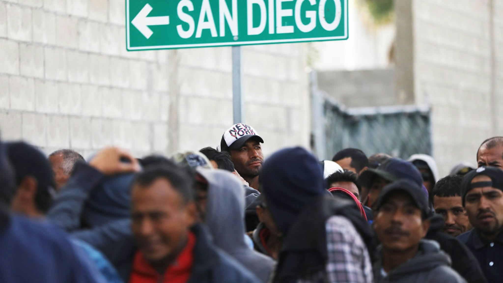 TIJUANA, MEXICO - MARCH 09: Migrants line up for free breakfast at the Desayunador Salesiano Padre Chava shelter and soup kitchen in front of sign for San Diego on March 9, 2018 in Tijuana, Mexico. The soup kitchen receives between 1,000-1,200 migrants daily, most of whom have been deported from the United States. Deportees sometimes end up homeless on the streets of Tijuana. (Photo by Mario Tama/Getty Images)