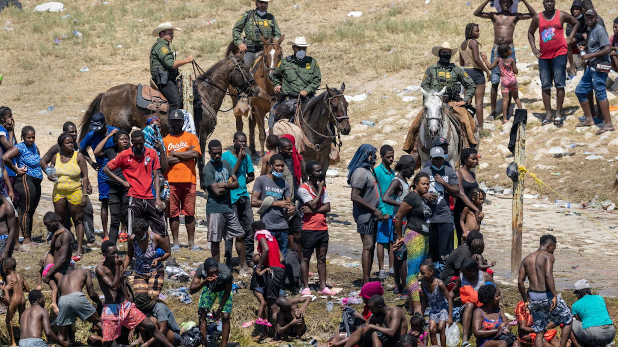 CIUDAD ACUNA, MEXICO - SEPTEMBER 20: Mounted U.S. Border Patrol agents watch Haitian immigrants on the bank of the Rio Grande in Del Rio, Texas on September 20, 2021 as seen from Ciudad Acuna, Mexico. As U.S. immigration authorities began deporting immigrants back to Haiti from Del Rio, thousands more waited in a camp under an international bridge in Del Rio while others crossed the river back into Mexico to avoid deportation. (Photo by John Moore/Getty Images)