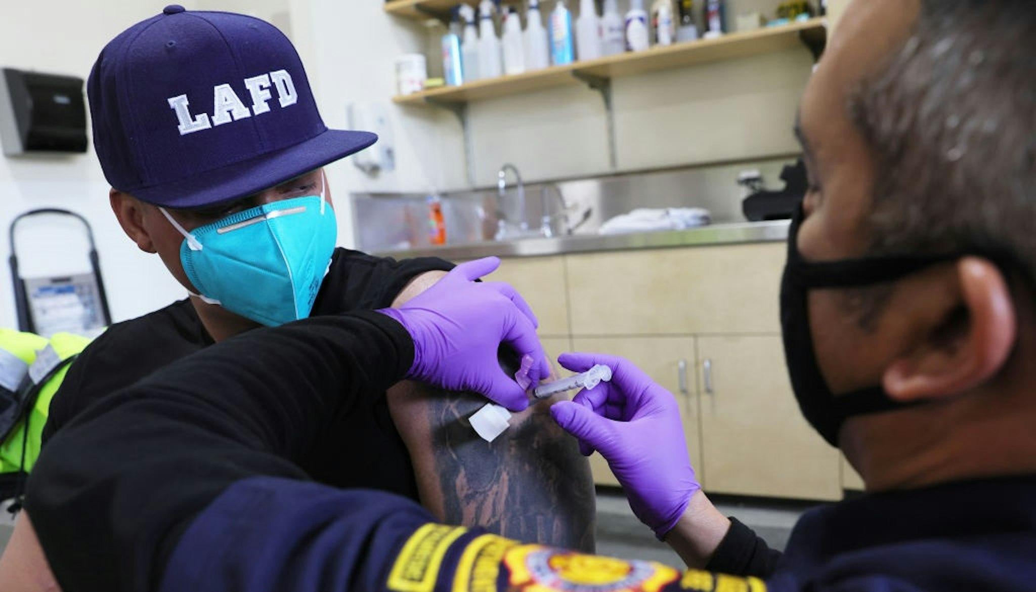 LOS ANGELES, CALIFORNIA - JANUARY 29: A Los Angeles Fire Department (LAFD) firefighter receives a COVID-19 vaccination dose from firefighter paramedic Alexander Gorme (R) at a fire station on January 29, 2021 in Los Angeles, California.