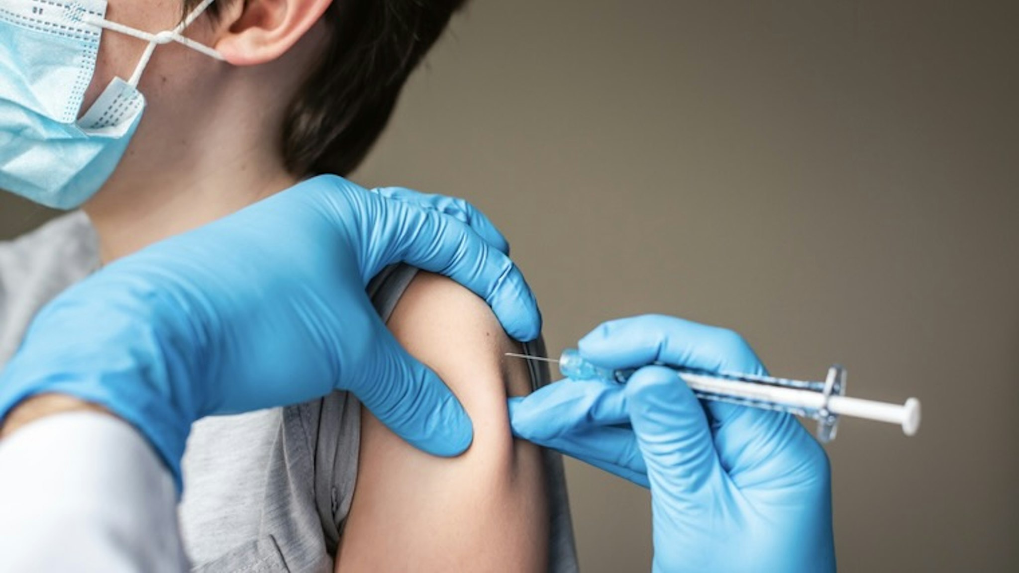 Child wearing mask getting vaccinated by doctor holding a needle. - stock photo Cavan Images via Getty Images