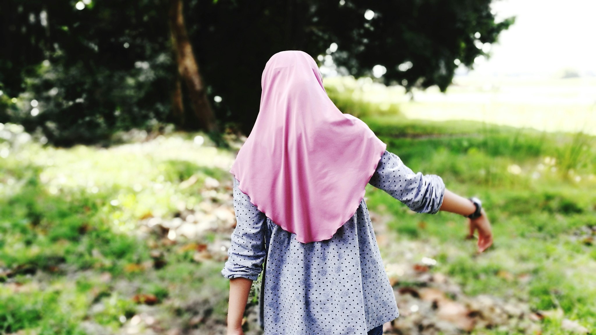 Rear View Of Girl Wearing Hijab Walking On Field - stock photo
