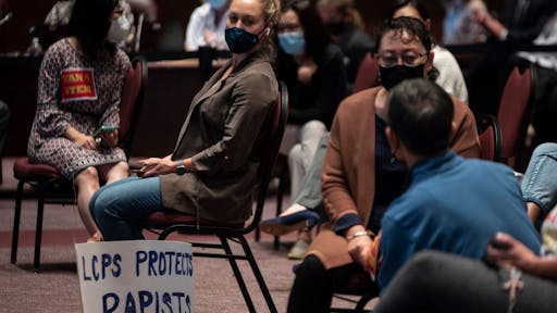 US-EDUCATION-SCHOOL A woman sits with her sign during a Loudoun County Public Schools (LCPS) board meeting in Ashburn, Virginia on October 12, 2021.