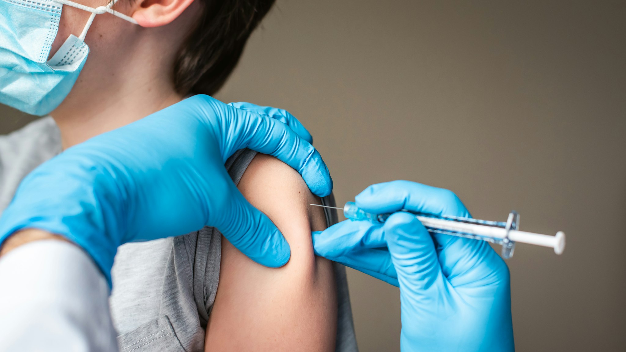 Child wearing mask getting vaccinated by doctor holding a needle. - stock photo
