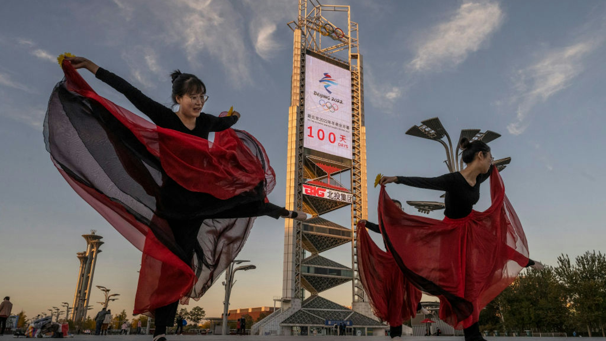 BEIJING, CHINA - OCTOBER 27: Women practice a dance routine in front of a large countdown screen showing 100 days before the opening of the Beijing 2022 Winter Olympics at the Olympic Park on October 27, 2021 in Beijing, China. The games are set to open on February 4, 2022. (Photo by Kevin Frayer/Getty Images)