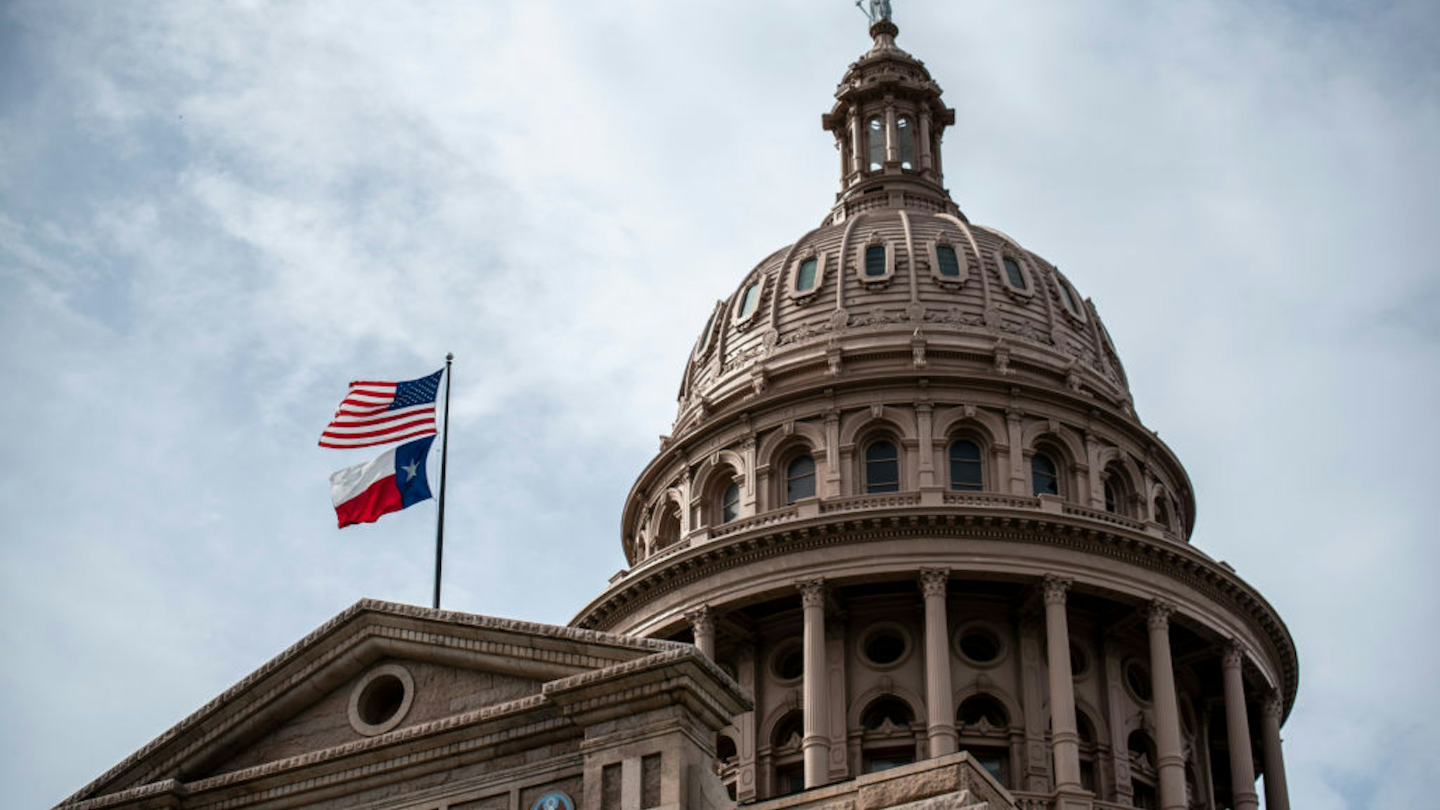 AUSTIN, TX - JULY 12: The U.S. and Texas state flags fly over the state Capitol building on July 12, 2021 in Austin, Texas. Texas Democrats have fled the state in order to prevent a quorum in protest over a Republican voting protection bill that they say is too restrictive.