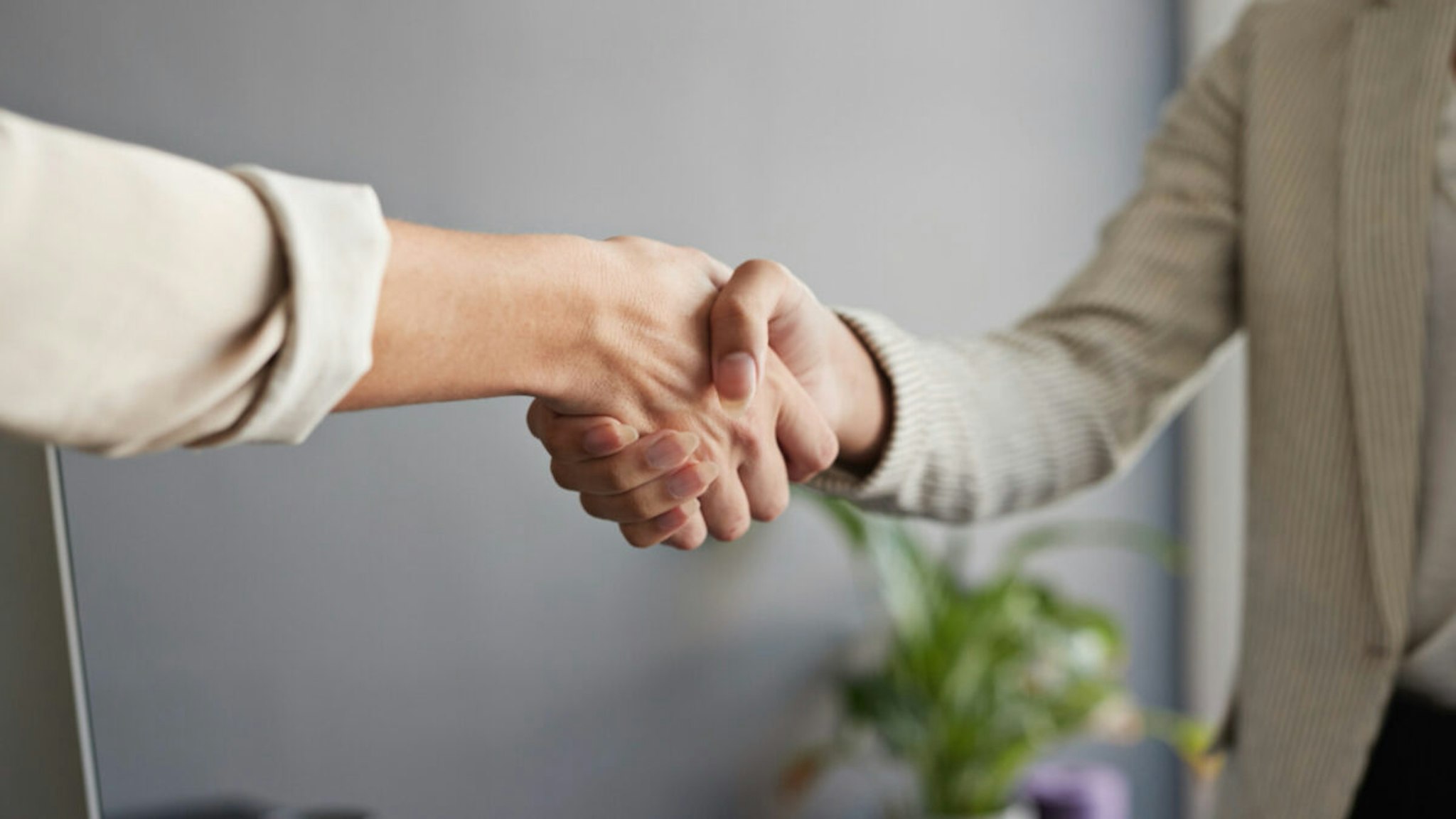 Midsection of female entrepreneur shaking hands with coworker at workplace.