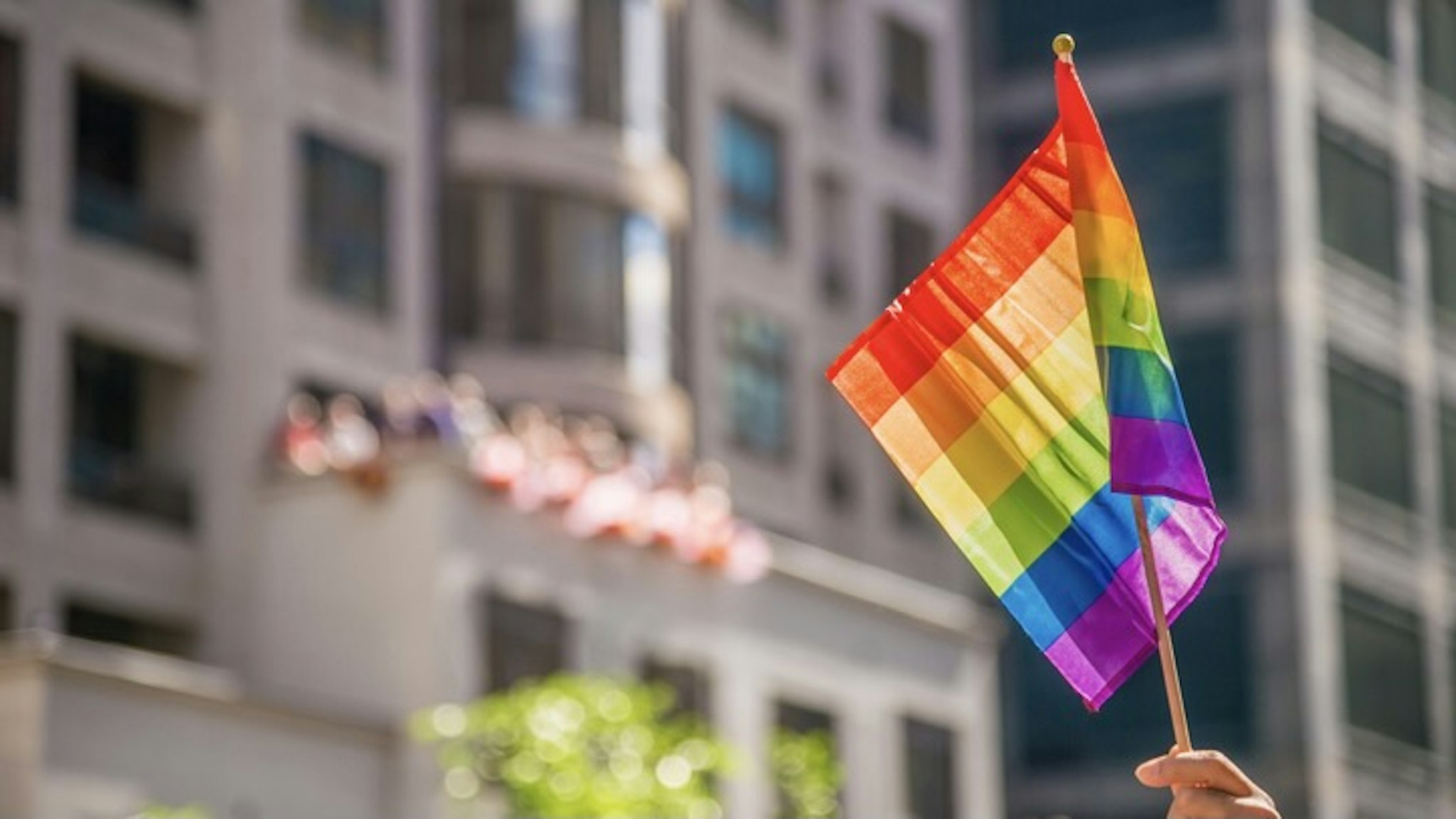 Cropped Hand Holding Rainbow Flag In City - stock photo Marc Bruxelle / EyeEm via Getty Images