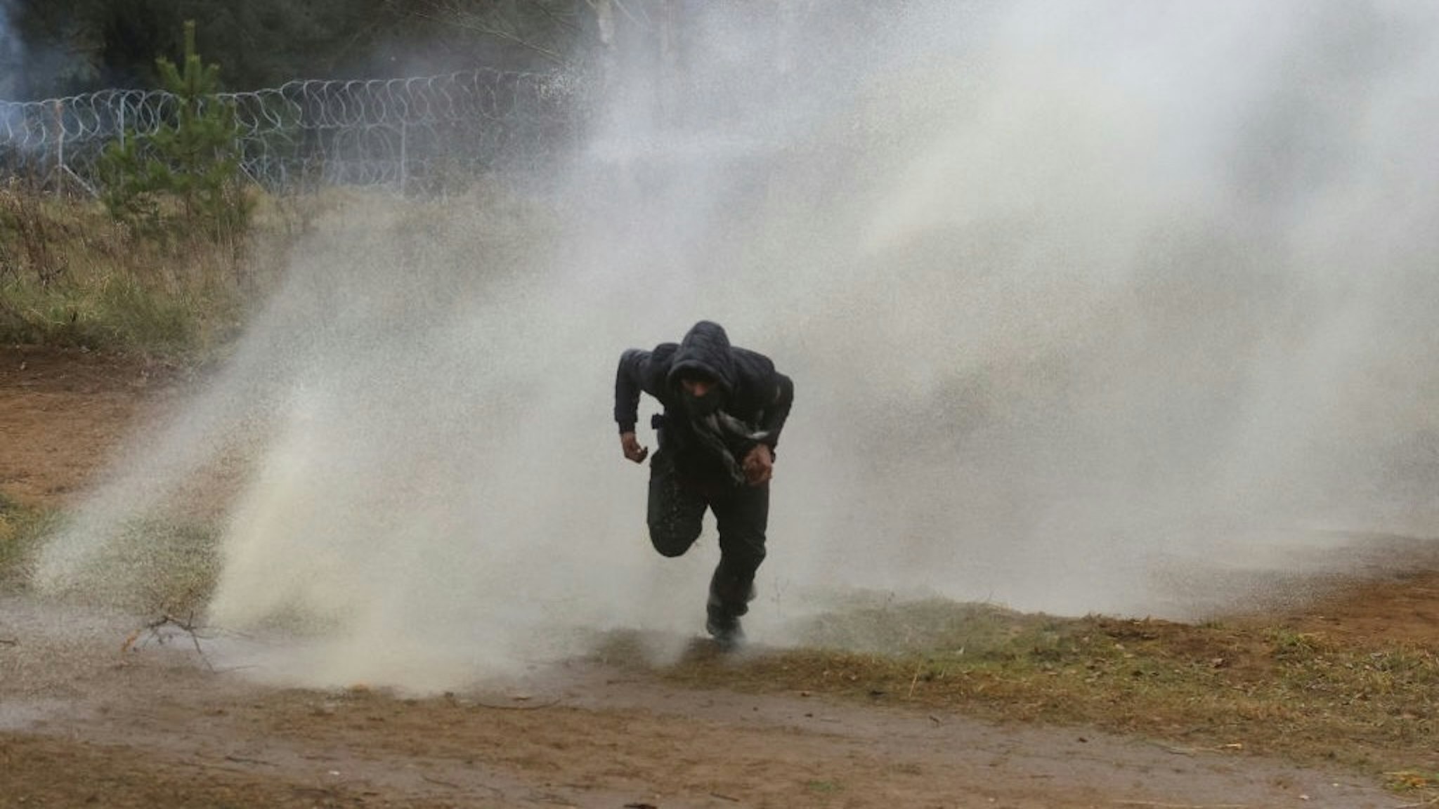 TOPSHOT-BELARUS-POLAND-EU-MIGRANTS TOPSHOT - A man runs away from a water cannon used by Polish law enforcement officers against migrants attempting to break into Poland at the Bruzgi-Kuznica border crossing on the Belarusian-Polish border on November 16, 2021. - - Belarus OUT (Photo by Leonid SHCHEGLOV / BELTA / AFP) / Belarus OUT (Photo by LEONID SHCHEGLOV/BELTA/AFP via Getty Images) LEONID SHCHEGLOV / Contributor