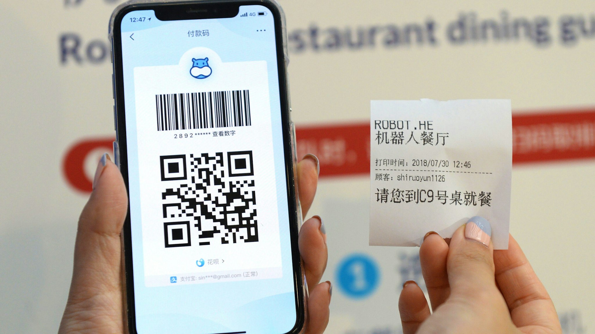 This photo taken on July 30, 2018 shows a QR code for payment on a smartphone and a receipt with booking information at the ROBOT.HE restaurant in Shanghai. - The little robotic waiter wheels up to the table, raises its glass lid to reveal a steaming plate of local Shanghai-style crayfish and announces in low, mechanical tones, "Enjoy your meal."