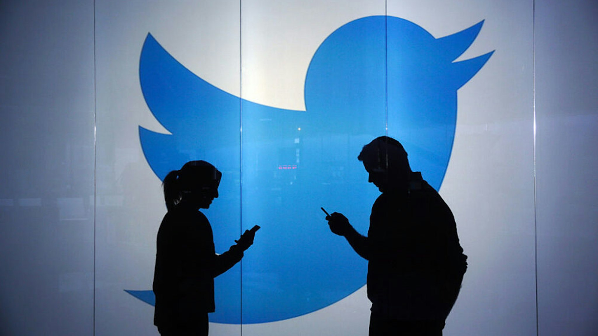 People are seen as silhouettes as they check mobile devices whilst standing against an illuminated wall bearing Twitter Inc.'s logo in this arranged photograph in London, U.K., on Tuesday, Jan. 5, 2016. Twitter Inc. may be preparing to raise its character limit for tweets to the thousands from the current 140, a person with knowledge of the matter said.