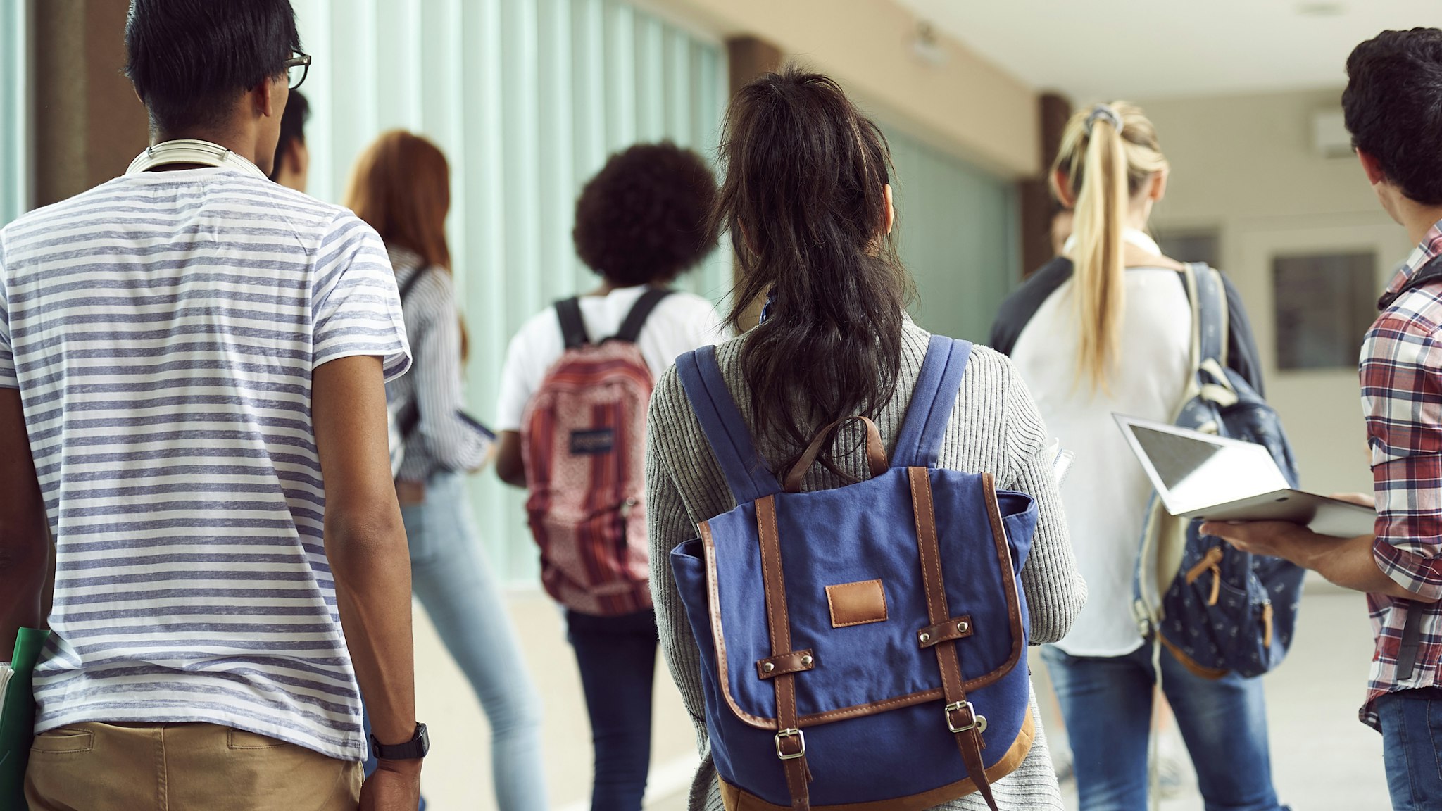 Students walking in school corridor, rear view