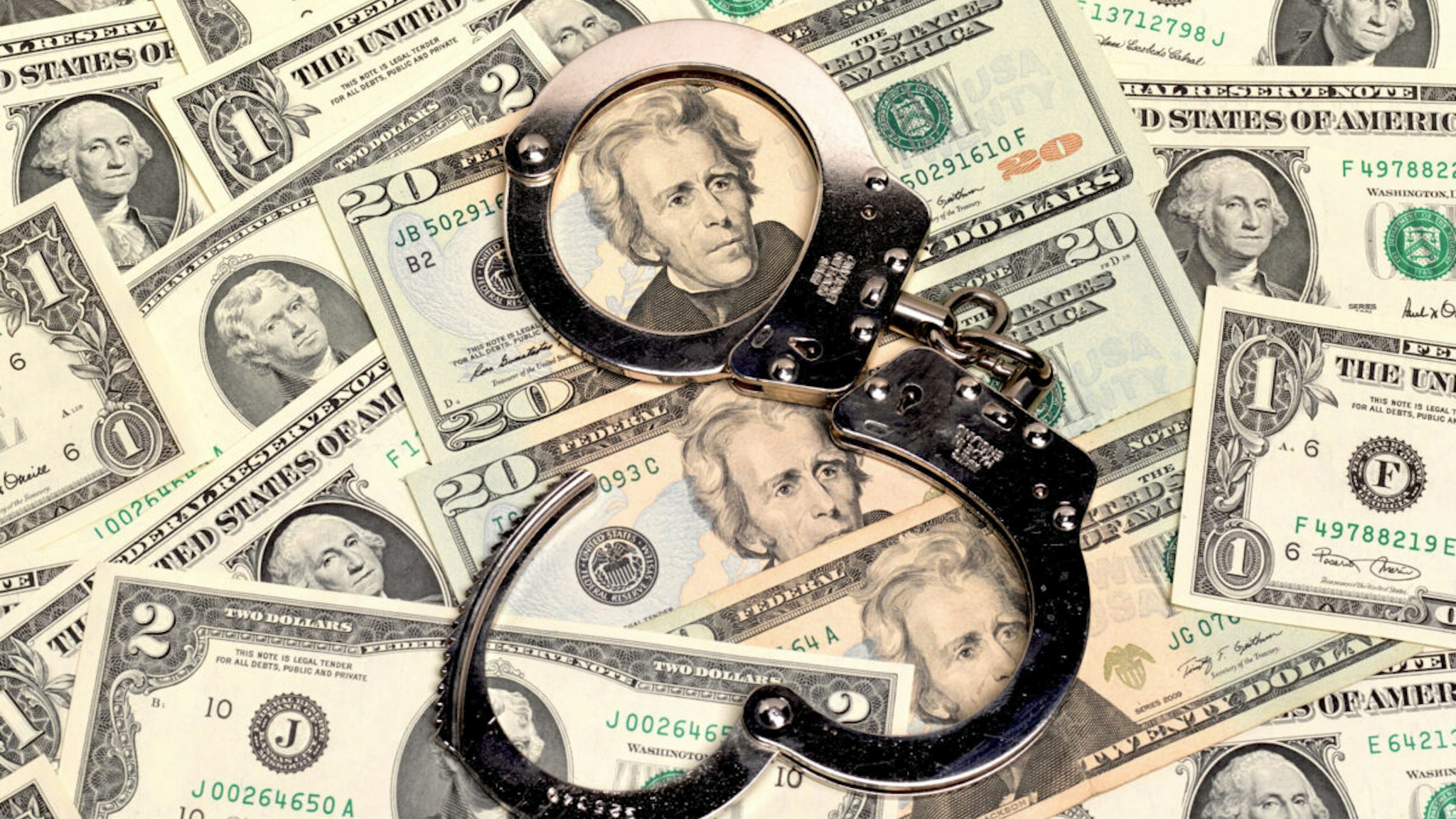 a pair of open handcuffs sitting on top of a pile of us dollars of assorted denominations