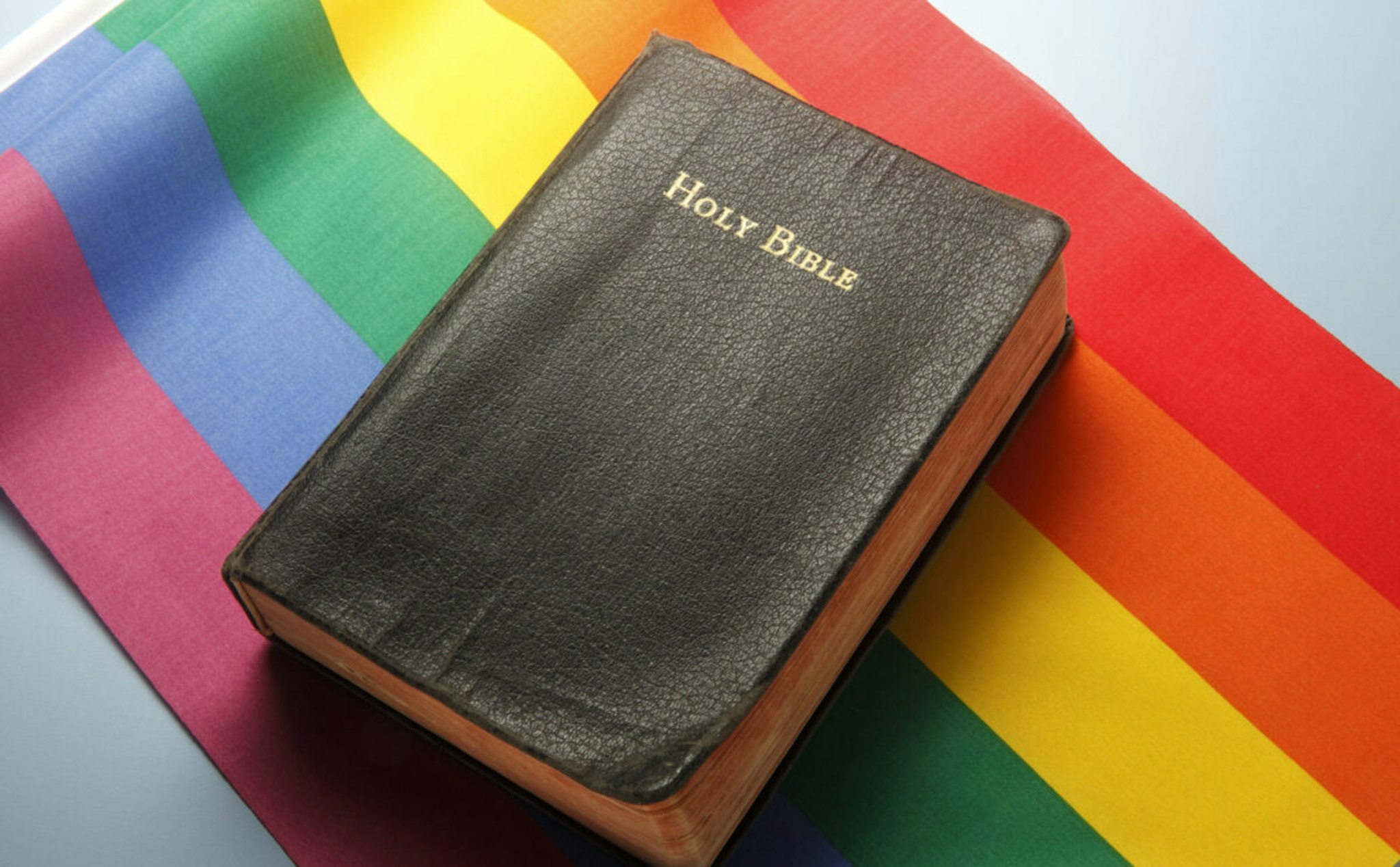 A Holy Bible sitting on top of a rainbow flag illustrating the conflicts between religion and LGBT issues.