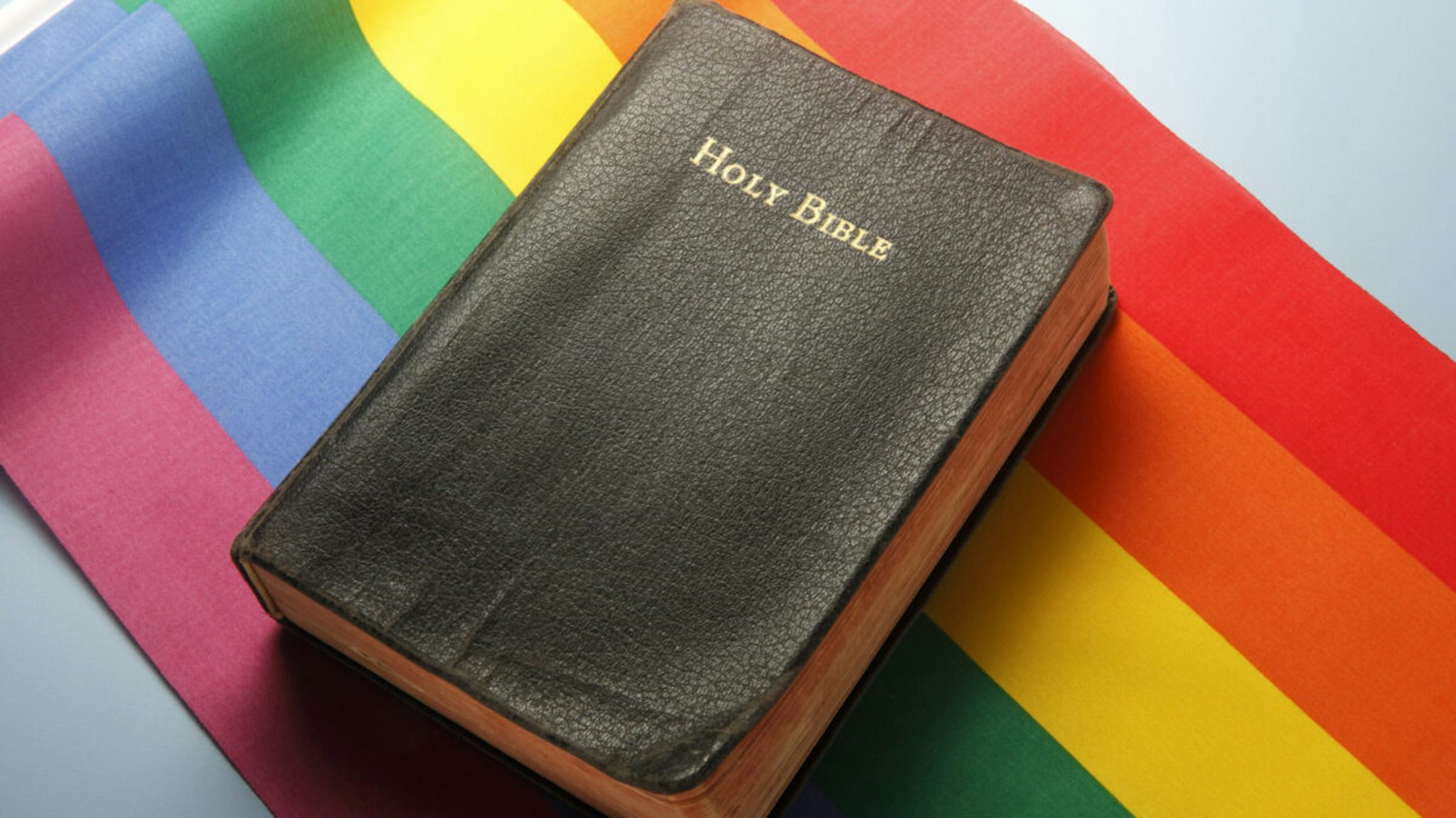 A Holy Bible sitting on top of a rainbow flag illustrating the conflicts between religion and LGBT issues.