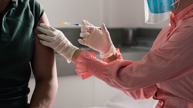 Southeast Asian female doctor giving vaccine shot on her male patient in a medical clinic - stock photo