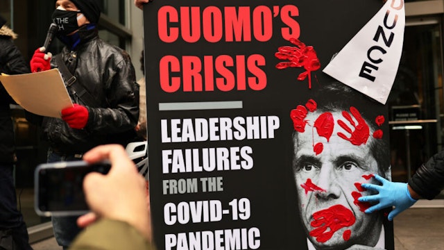 NEW YORK, NEW YORK - MARCH 01: A person places his red painted hands on a poster of Gov. Andrew Cuomo's book as people gather outside of his NYC office to protest against cuts to health care on March 01, 2021 in New York City. On the one-year anniversary of the first coronavirus (COVID-19) diagnosis in NYC, grassroots organizations gathered as part of the “Invest In Our NY campaign!” demanding Gov. Cuomo and NYS lawmakers stop the cuts from HIV/AIDS and other healthcare service and pass bills that would raise revenue and help to restore money to Medicaid, cancel rent for low-income New Yorkers and protect vulnerable communities.