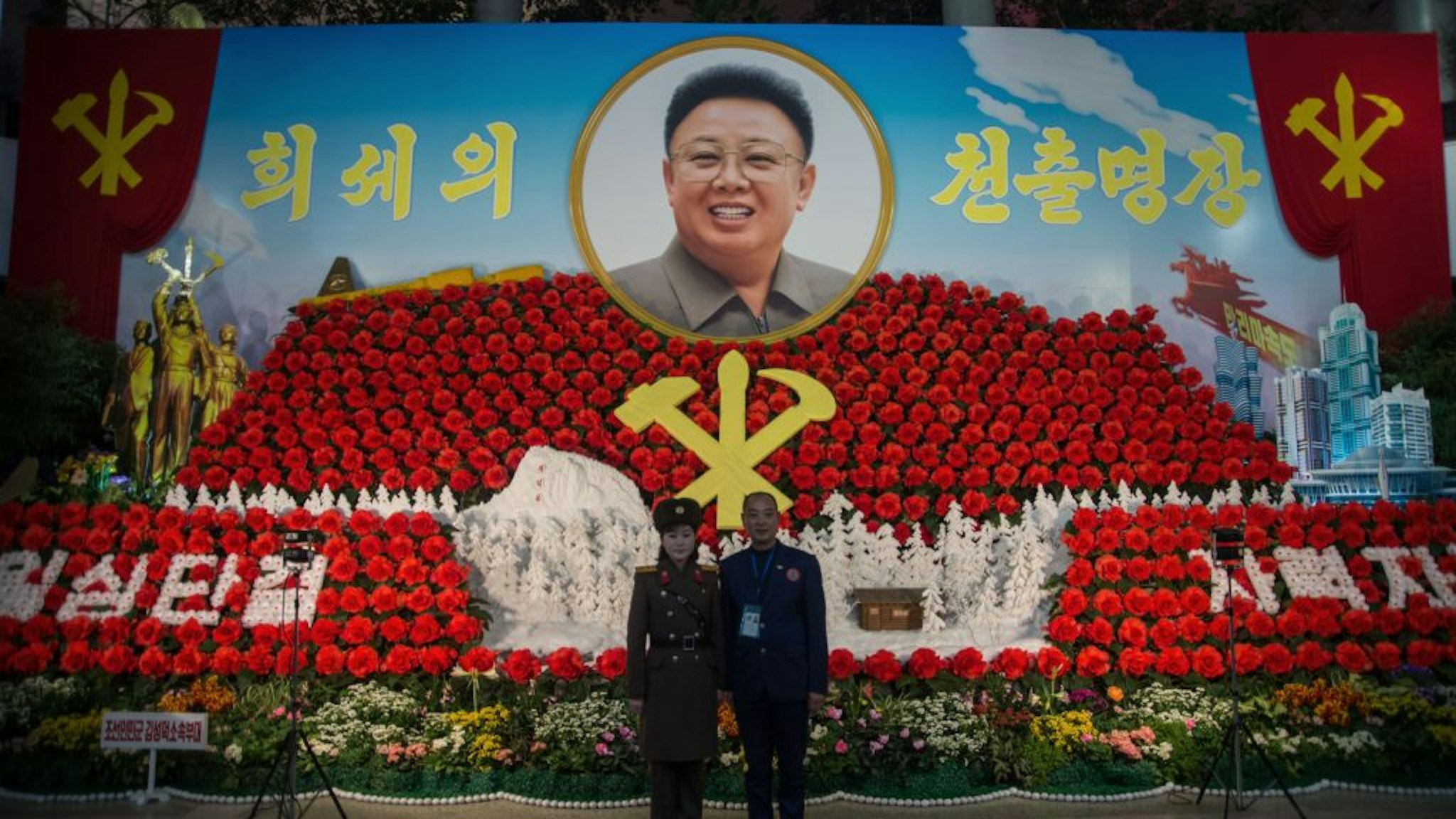 A foreign visitor (R) stands for a photo with a Korean People's Army (KPA) soldier in front of a portrait of late North Korean leader Kim Jong IL, at the 22nd 'Kimjongilia Festival' flower festival marking the upcoming 'Day of Shining Star', the anniversary of the Kim's birth, in Pyongyang on February 13, 2018.