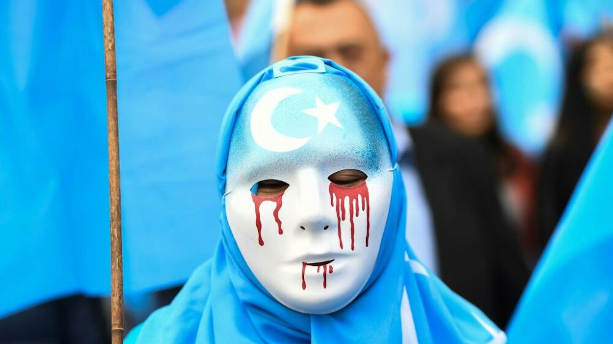 TOPSHOT - A person wearing a white mask with tears of blood takes part in a protest march of ethnic Uighurs asking for the European Union to call upon China to respect human rights in the Chinese Xinjiang region and ask for the closure of "re-education center" where Uighurs are detained, during a demonstration around the EU institutions in Brussels on April 27, 2018.