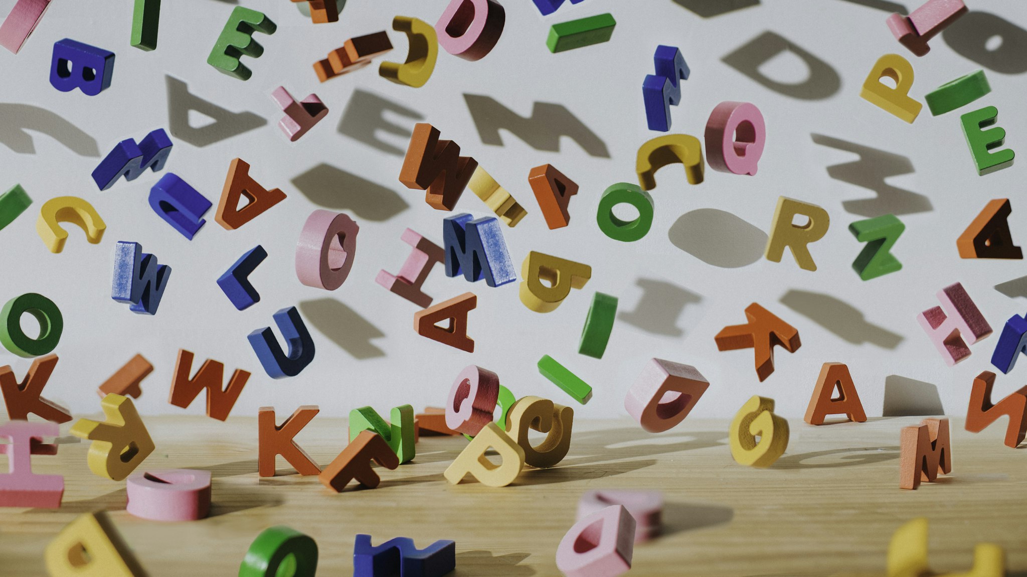Conceptual image of colourful falling letters, casting shadows on a white wall.