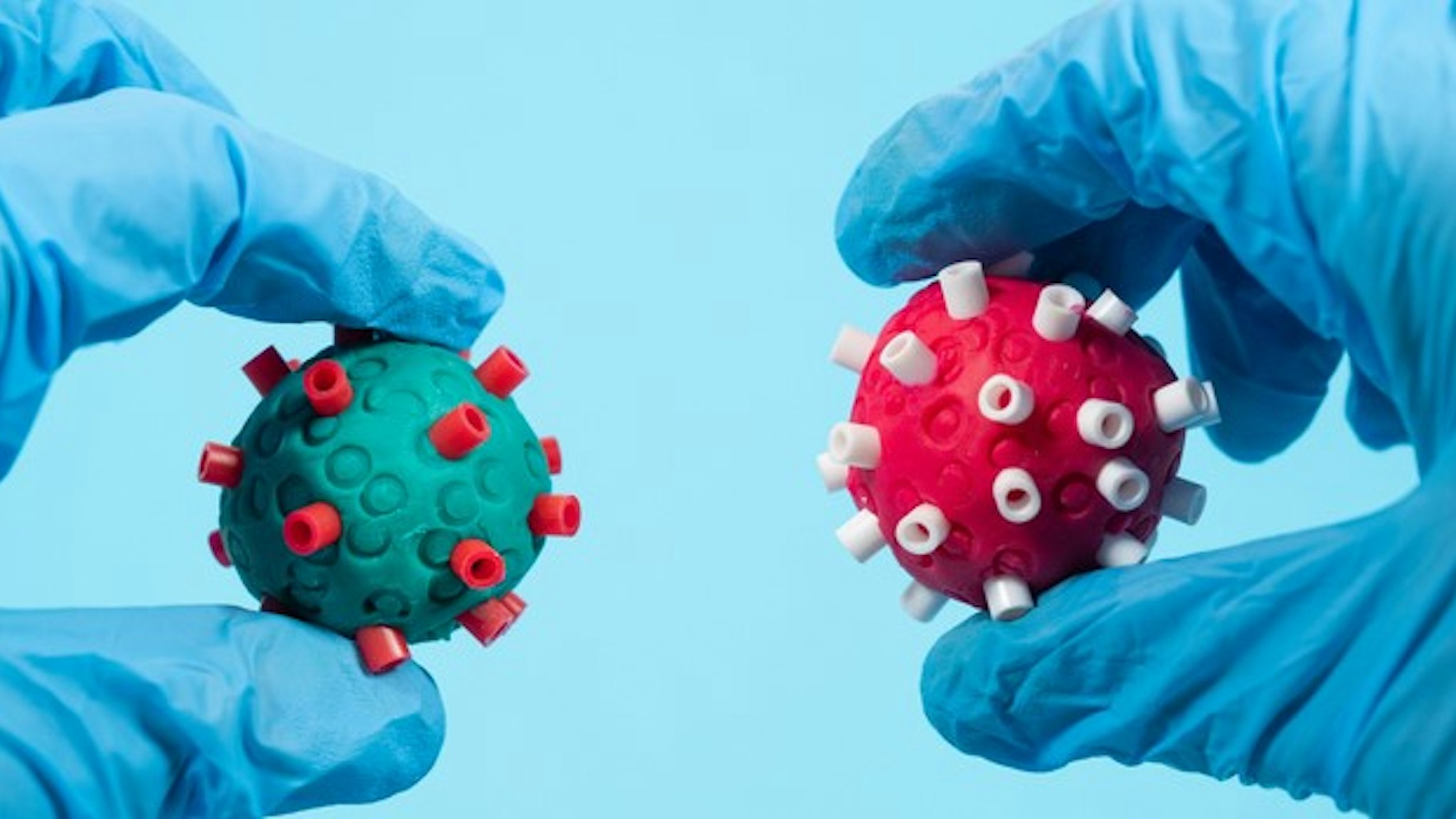 Scientists with surgical gloves holds two different Coronavirus of different color in the hand. Creative image.