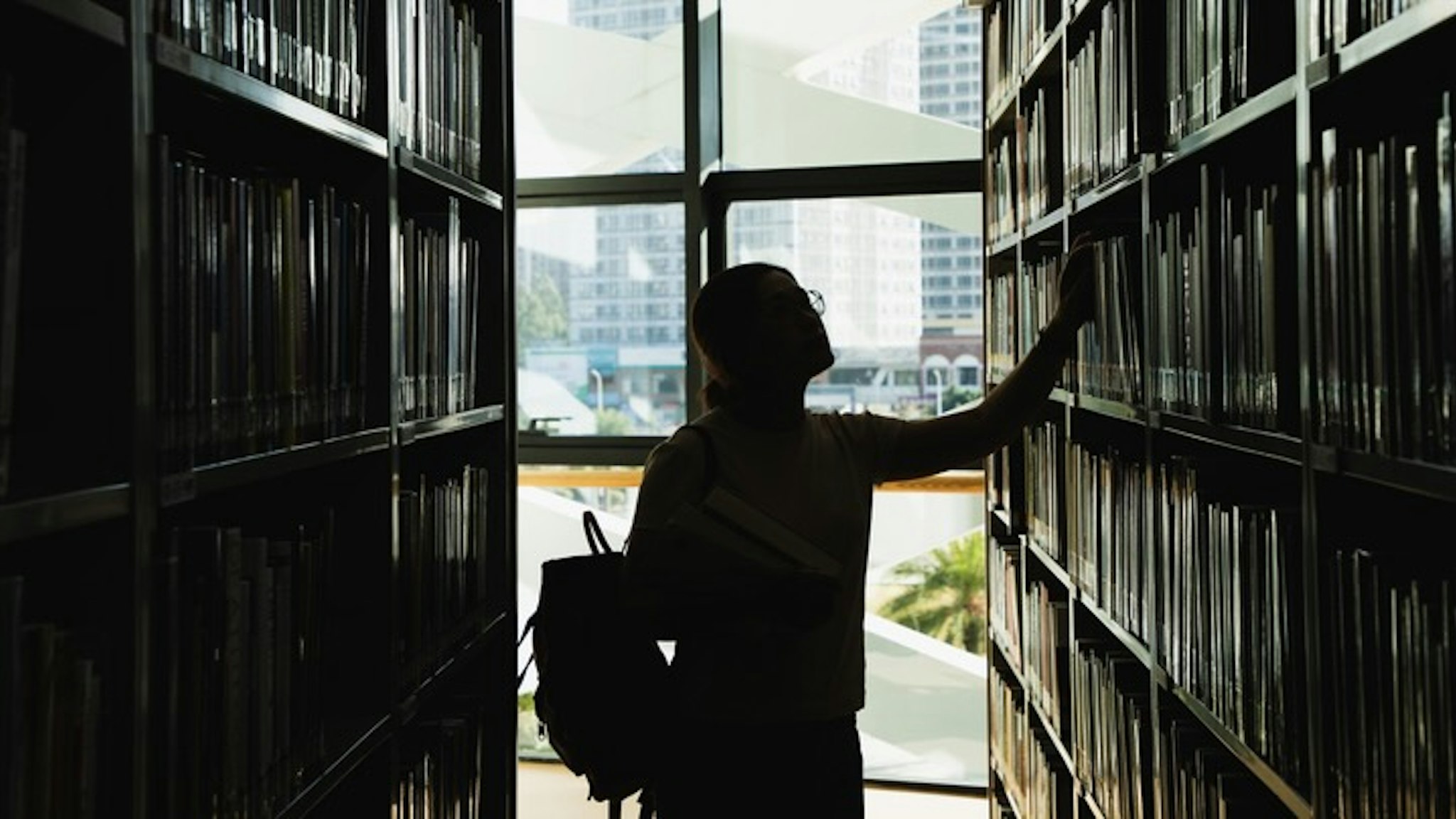 female student in silhouette looking at the books from the bookshelf - stock photo female student in silhouette looking at the books from the bookshelf Kilito Chan via Getty Images