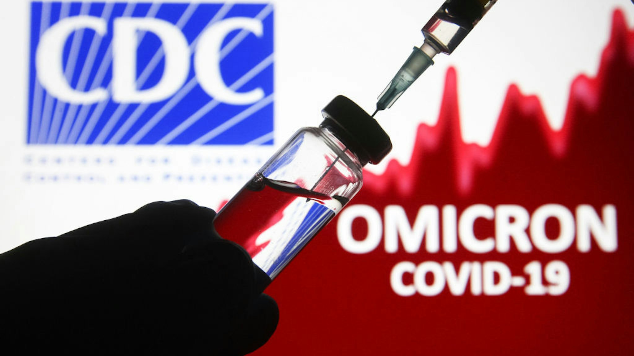 UKRAINE - 2021/12/05: In this photo illustration, a hand extracting a dose of vaccine from a vial is seen in front of the words Omicron covid-19 with a logo of CDC in the background.