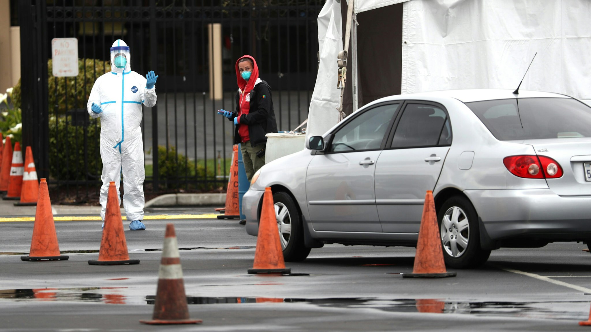 SAN MATEO, CALIFORNIA - MARCH 16: A medical worker guides a car that is going through a coronavirus drive-thru test clinic at the San Mateo County Event Center on March 16, 2020 in San Mateo, California. Drive-thru test clinics for COVID-19 are popping up across the country as more tests become available.