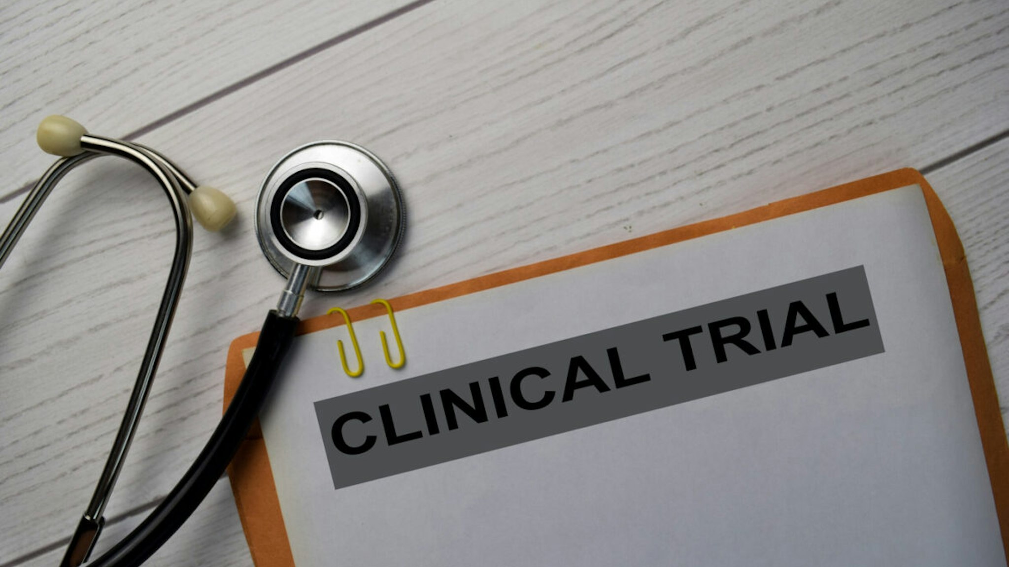 Clinical Trial text with document brown envelope and stethoscope isolated on office desk.