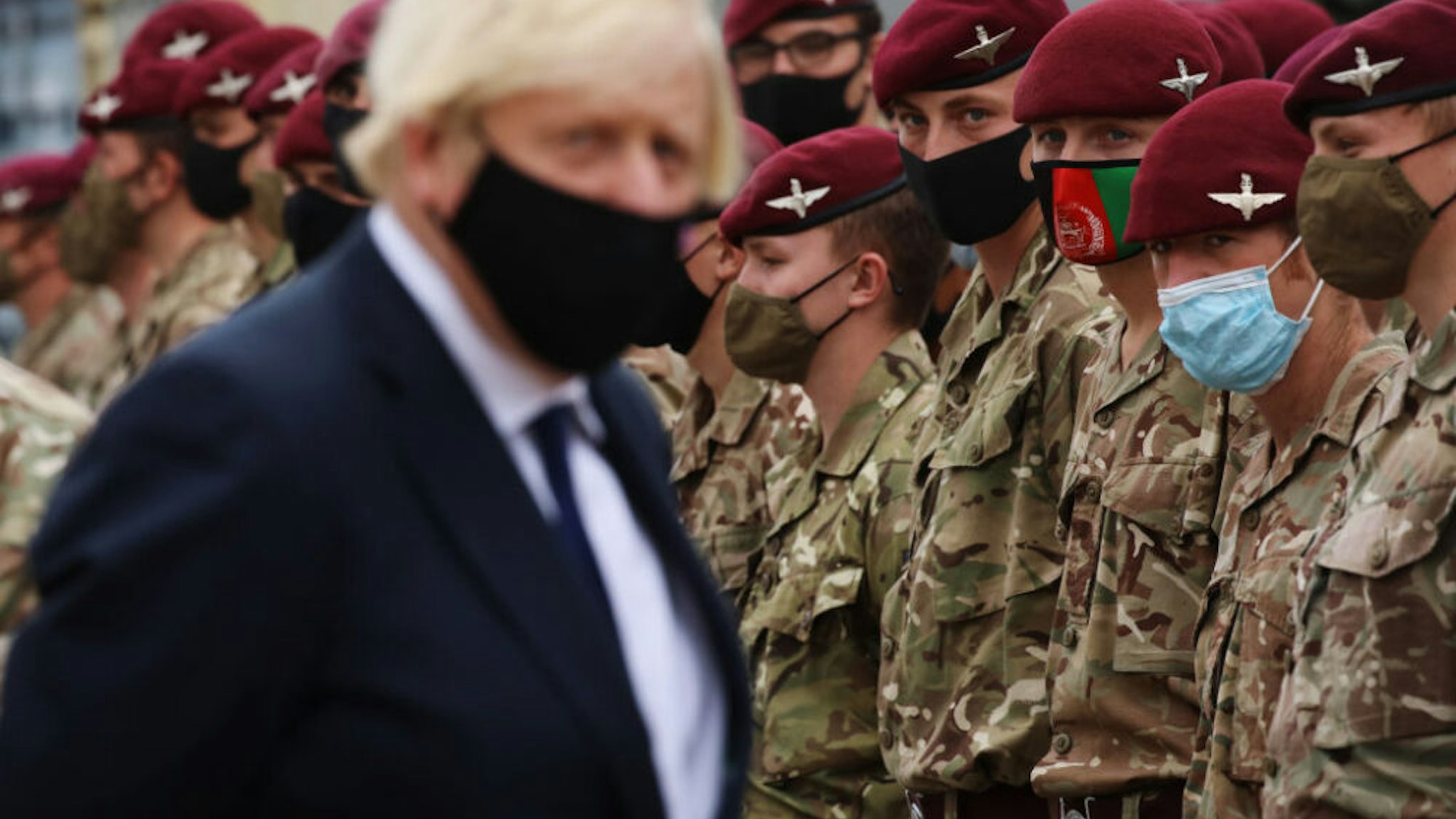 COLCHESTER, ENGLAND - SEPTEMBER 02: A soldier wearing a protective face mask depicting the flag of Afghanistan looks on as UK prime minister Boris Johnson meets with military personnel who worked on the Afghan evacuation during a visit to Merville Barracks on September 2, 2021 in Colchester, United Kingdom. Members of the 16th Air Assault Brigade worked with US forces to secure the Kabul airport for last month's evacuation operation.