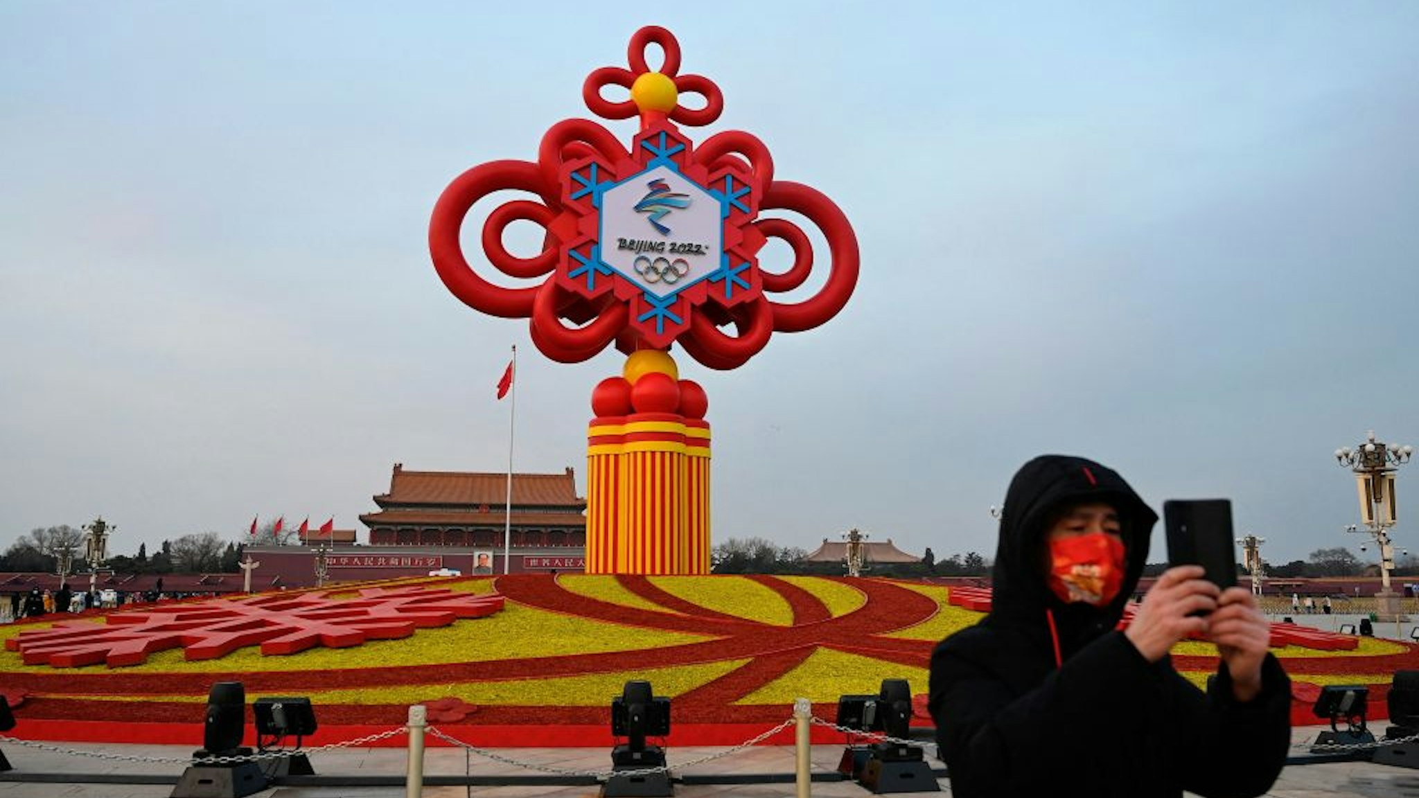 A man records video footage in front of an installation displaying a Chinese knot with the logo of the Beijing 2022 Winter Olympics at Tiananmen Square in Beijing on January 19, 2022. (Photo by JADE GAO / AFP) (Photo by JADE GAO/AFP via Getty Images)
