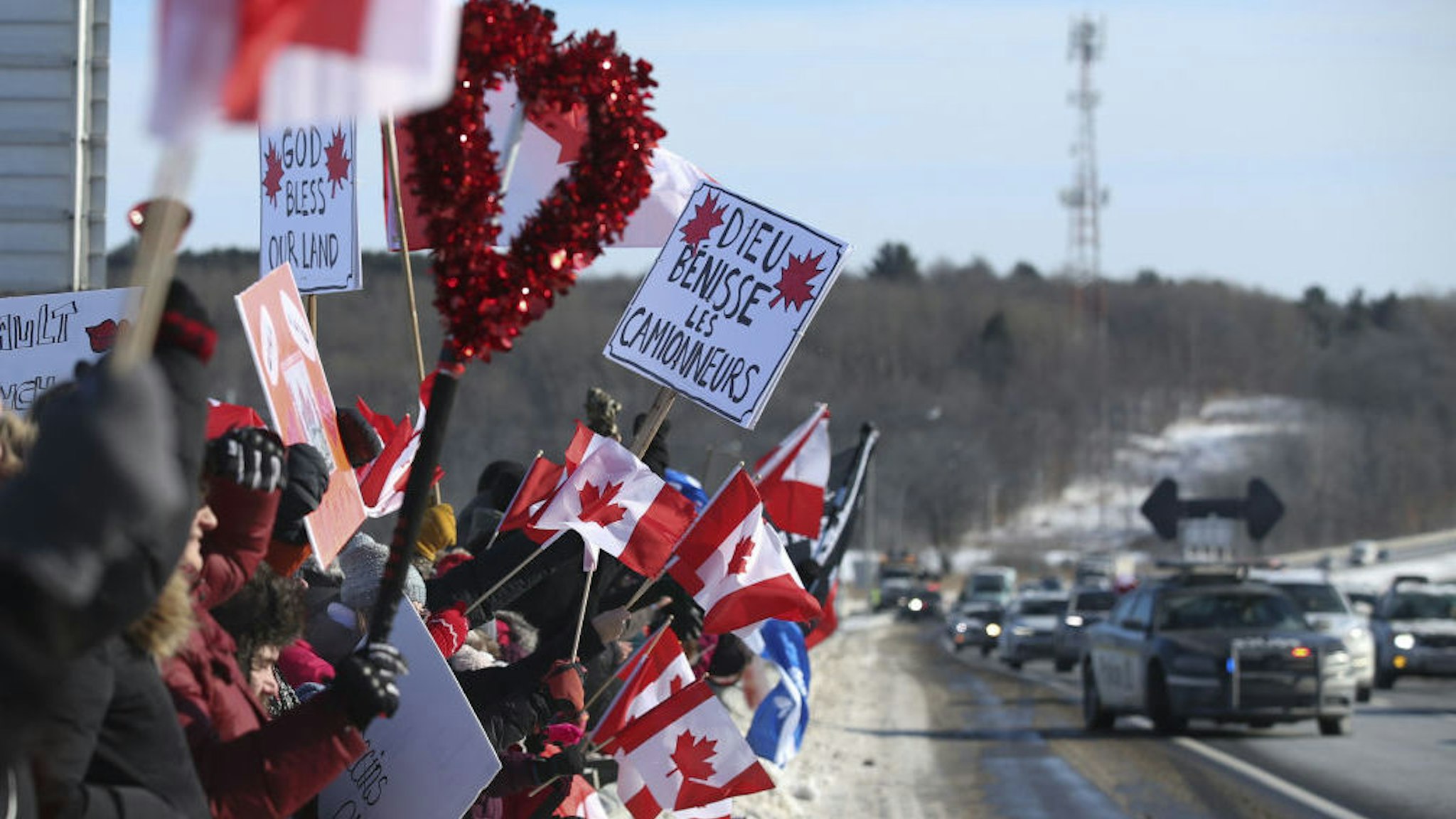 Supporters hold signs as a convoy of trucks passes on the highway in Rigaud, Quebec, Canada, on Friday, Jan. 28, 2022.