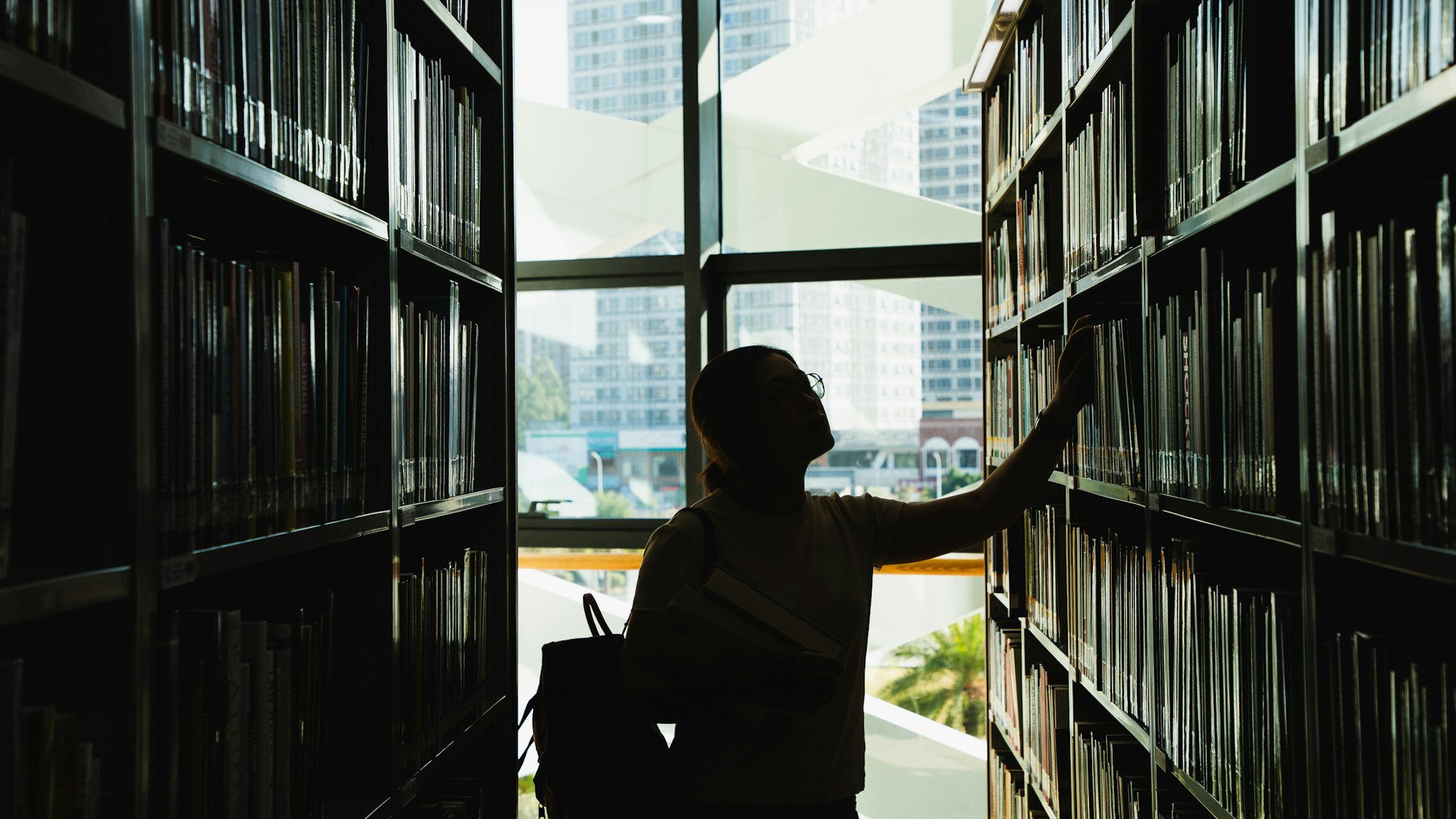 female student in silhouette looking at the books from the bookshelf - stock photo