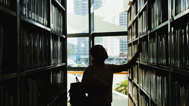 female student in silhouette looking at the books from the bookshelf - stock photo