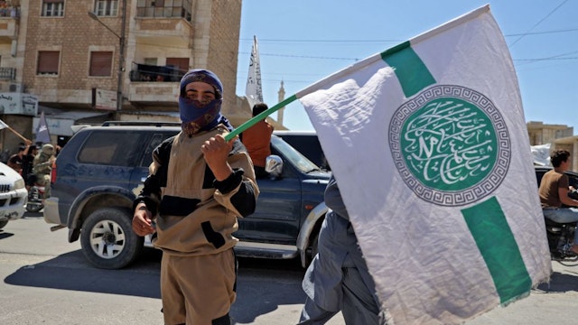 A member of Syria's top jihadist group the Hayat Tahrir al-Sham (HTS) alliance, led by Al-Qaeda's former Syria affiliate, holds the group's flag as others parade with their flags and those of the Taliban's declared "Islamic Emirate of Afghanistan" through the rebel-held northwestern city of Idlib on August 20, 2021. - The armed group that formally broke ties with al-Qaeda years ago is considered to be the most prominent jihadist group in Syria after a decade of war. HTS controls nearly half of the Idlib region -- the last remaining opposition bastion in Syria -- alongside other less influential groups.