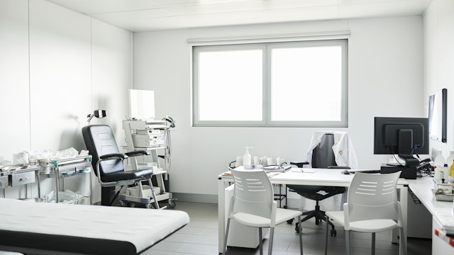 Furniture and medical equipment at doctor's office. Empty chairs are at desk in clinic during COVID-19. Interior of medical examination room.
