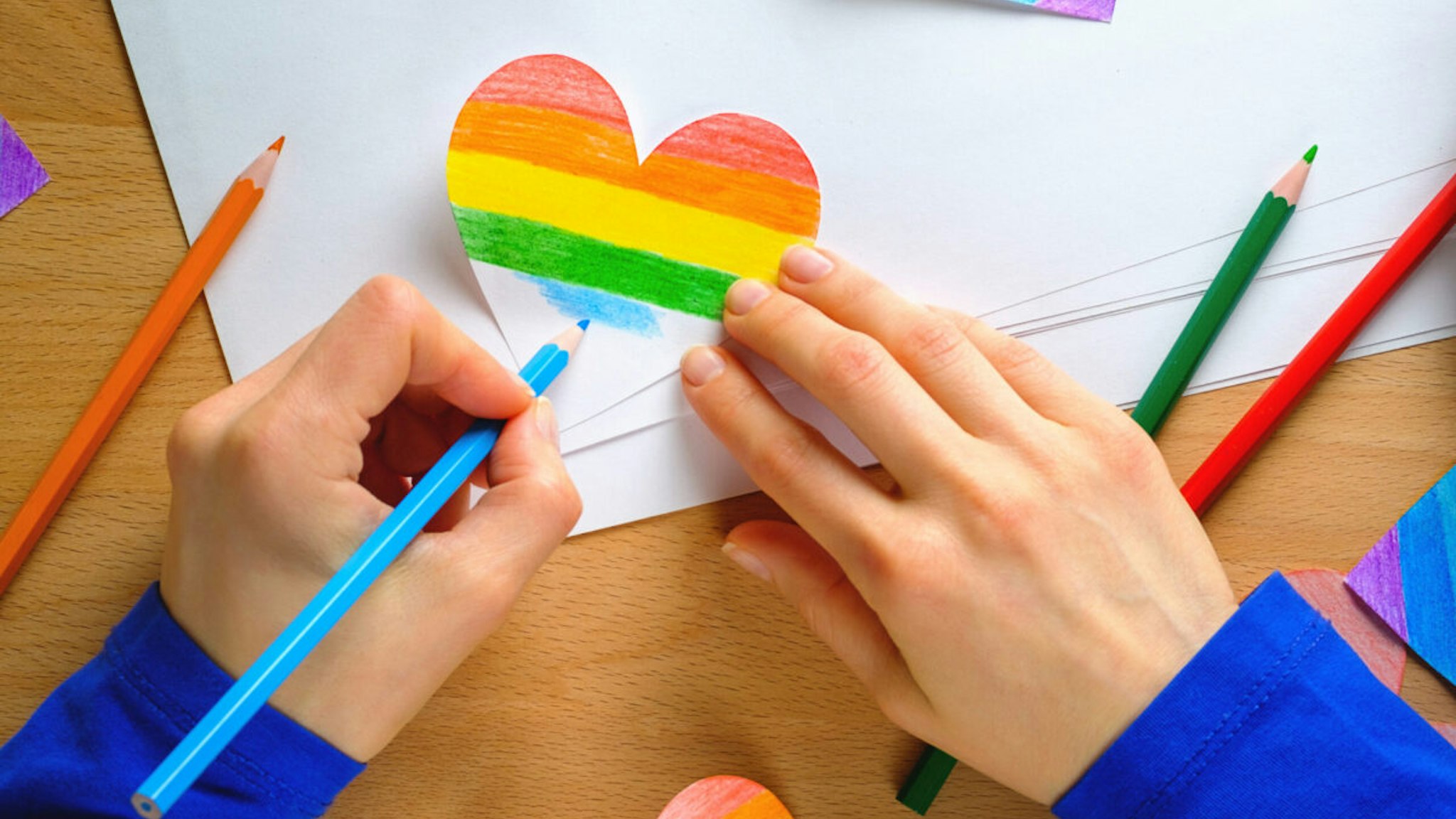 A girl or woman paints a Heart in the color of the LGBT flag.