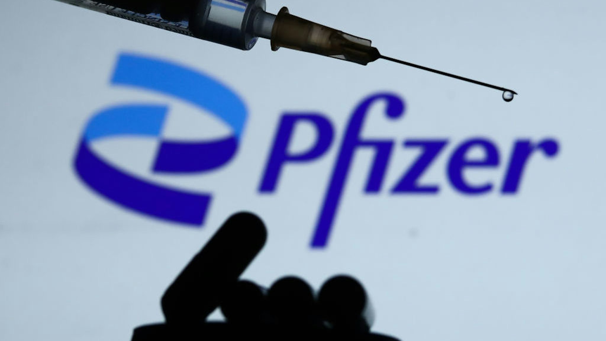 Medical syringe and medicine pills are seen with Pfizer logo in the background in this illustration photo taken in Krakow, Poland on December 14, 2021. (Photo by Jakub Porzycki/NurPhoto via Getty Images)